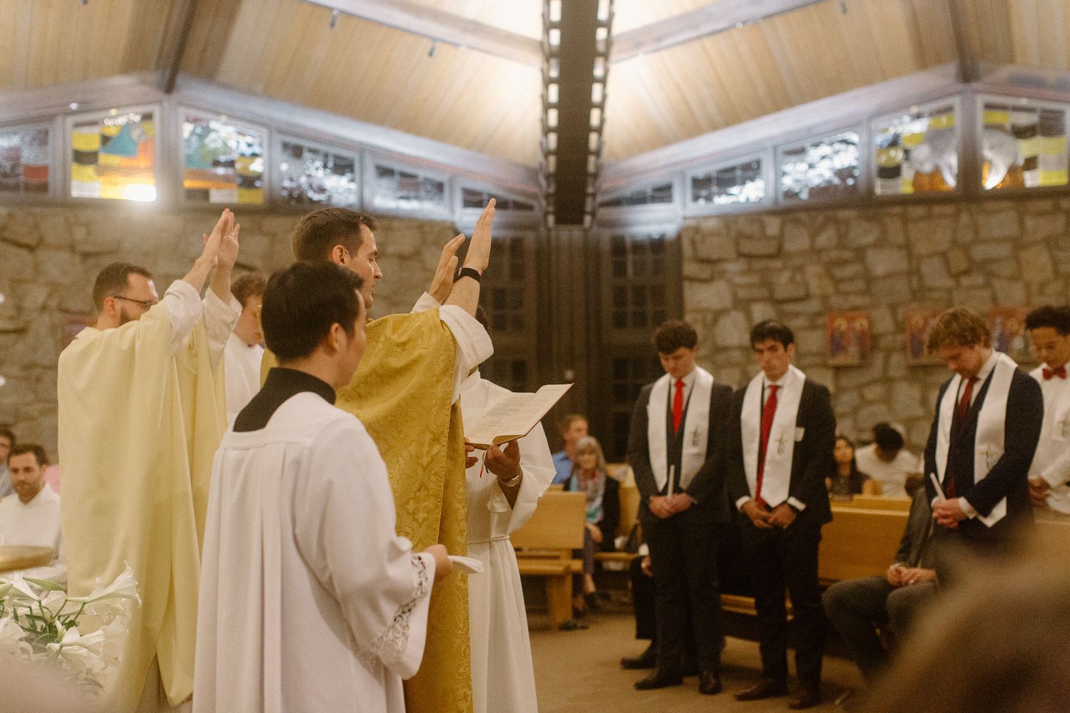 Catholic priests perform a blessing ceremony over young men in white robes inside a stone Catholic church in Athens, GA.
