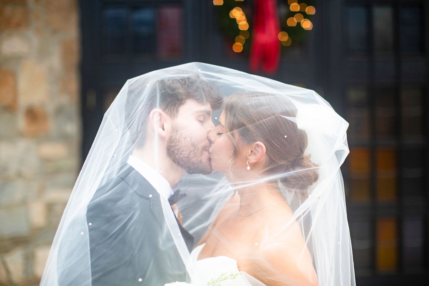 Bride and groom sharing a romantic kiss under a white wedding veil outdoors on their wedding day outside Catholic church in Athens, GA.