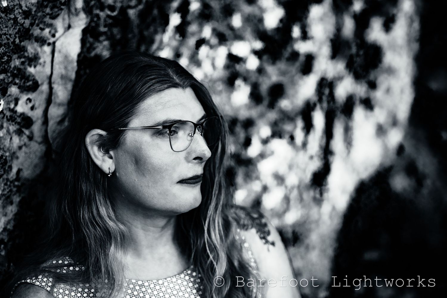 A portrait of a woman in black and white with glasses, stone behind her as she looks to the right.