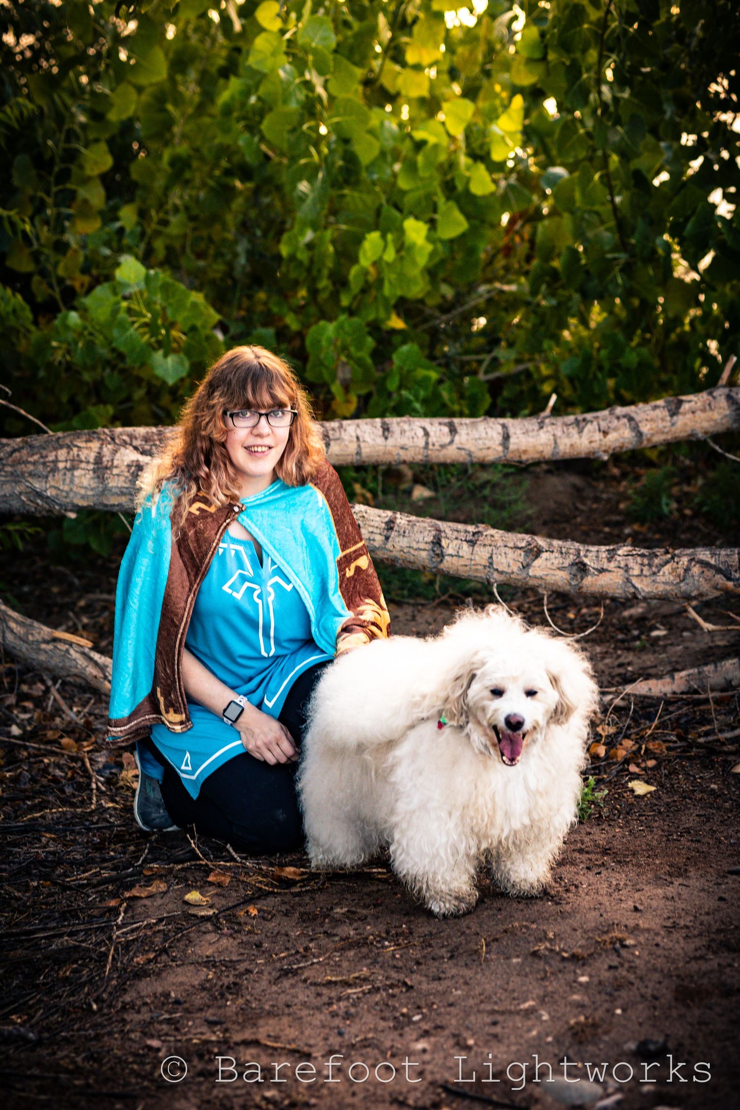 A photo of a woman with wavy blond hair and glasses with her dog in the morning sunlight.