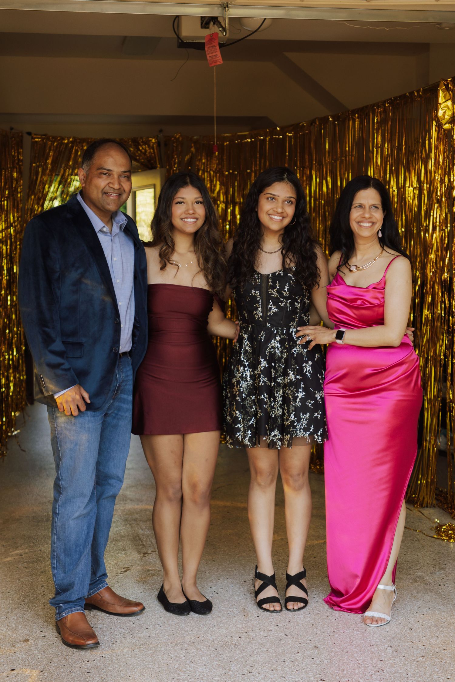 Family of four posing together at graduation party in front of gold tinsel fringe backdrop.