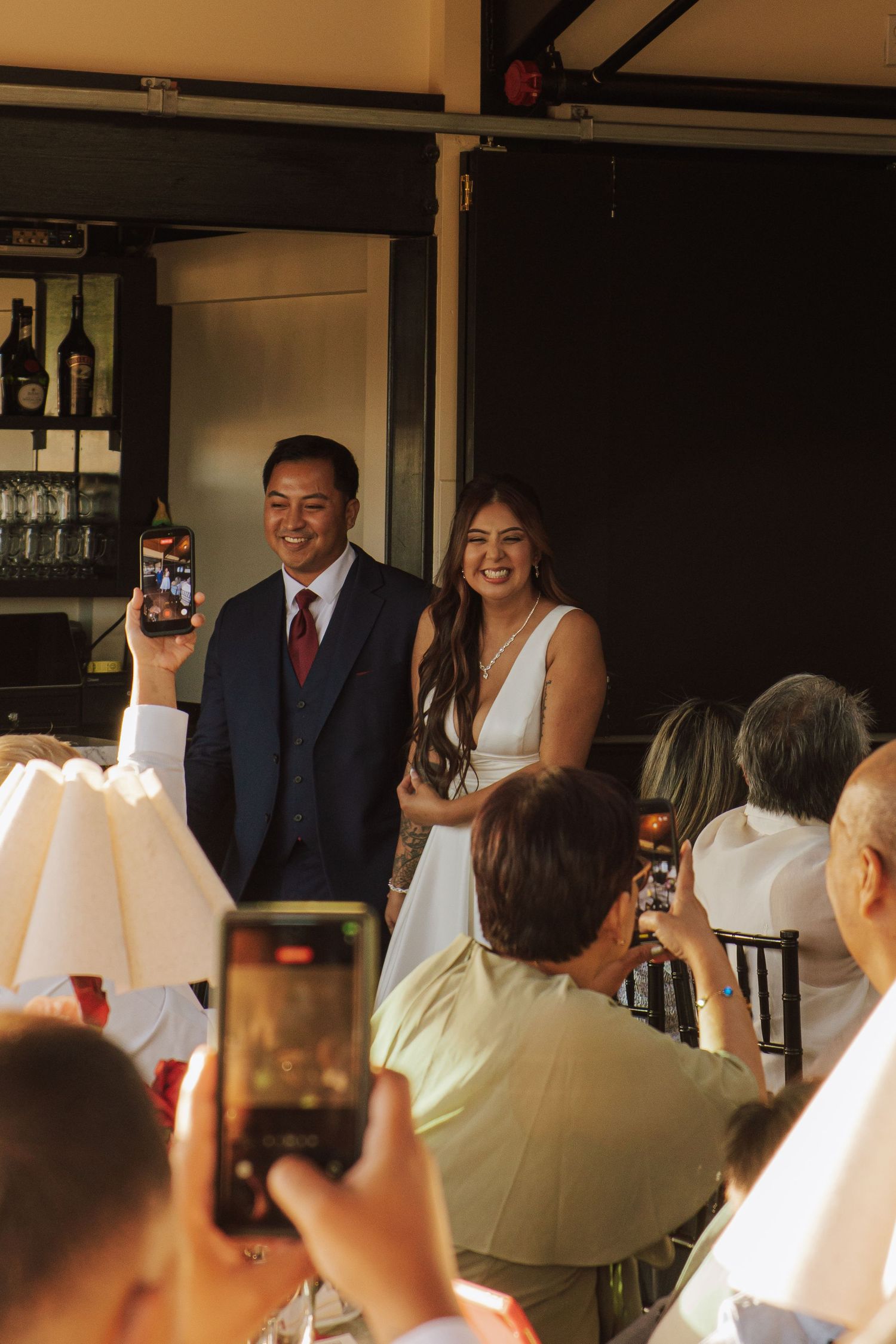 Bride and groom smile as guests photograph them during their wedding reception entrance celebration.