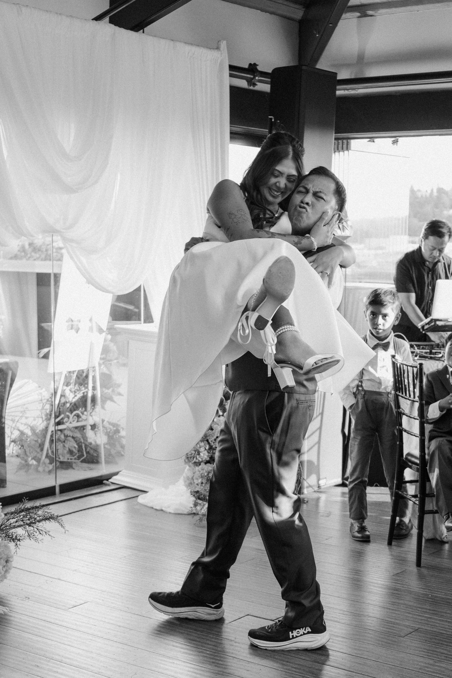 Groom lifts bride during joyful first dance at elegant wedding reception in black and white.