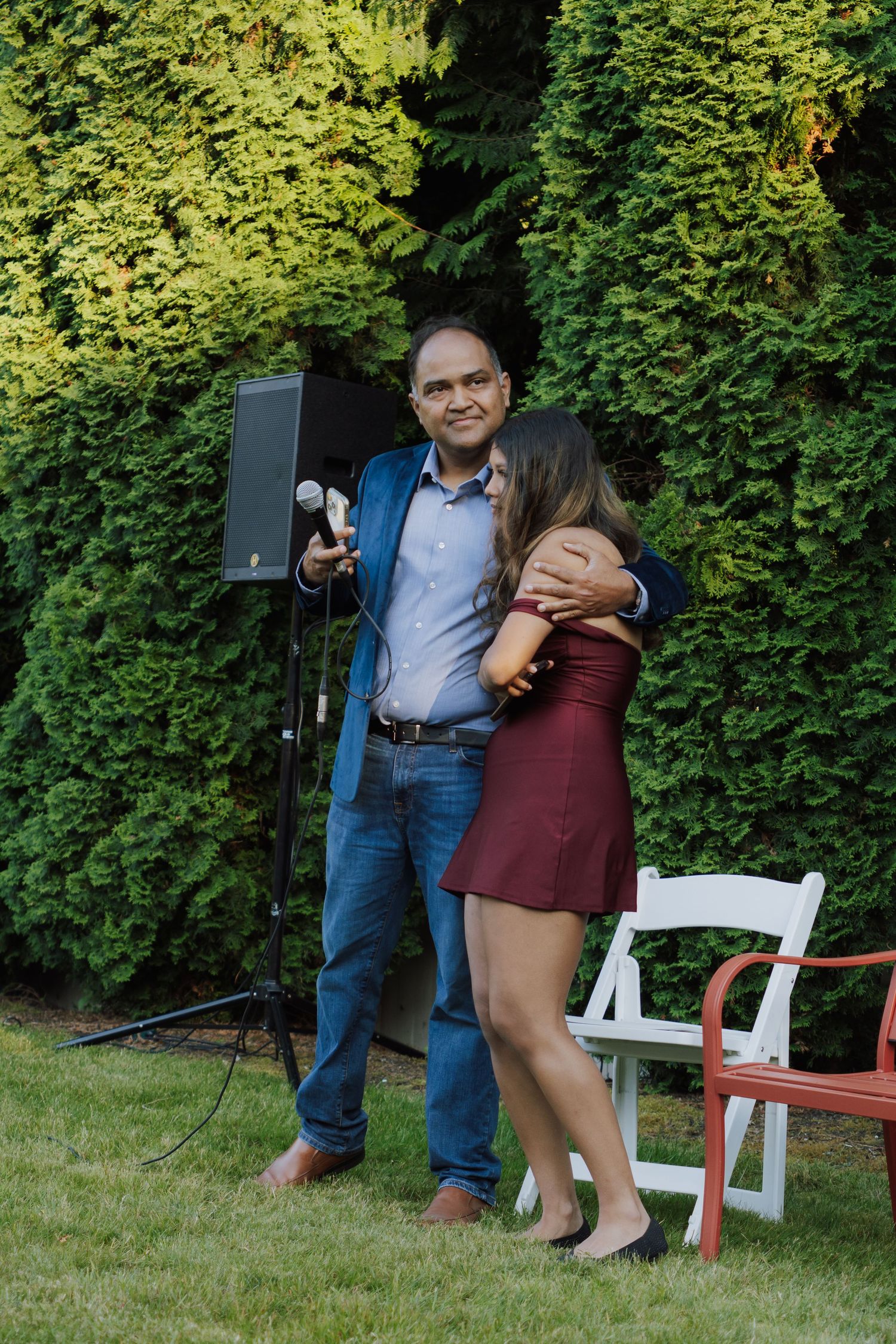 Man in blue blazer hugging young woman at outdoor graduation celebration party.