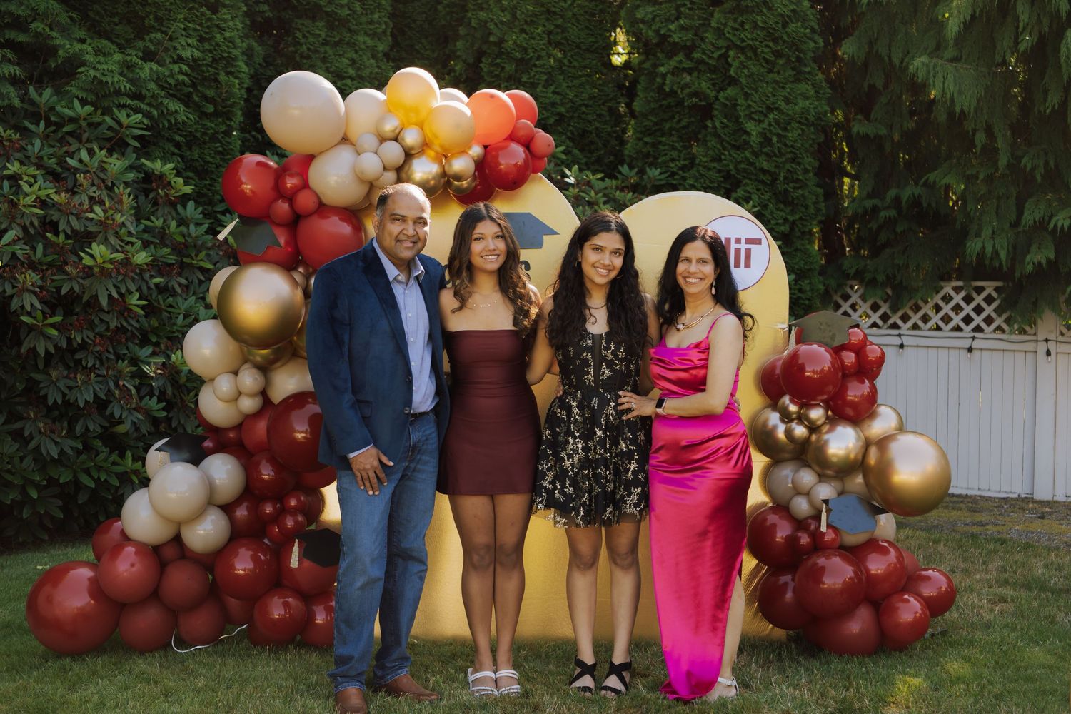 Family of four posing together in front of MIT graduation balloon arch display.