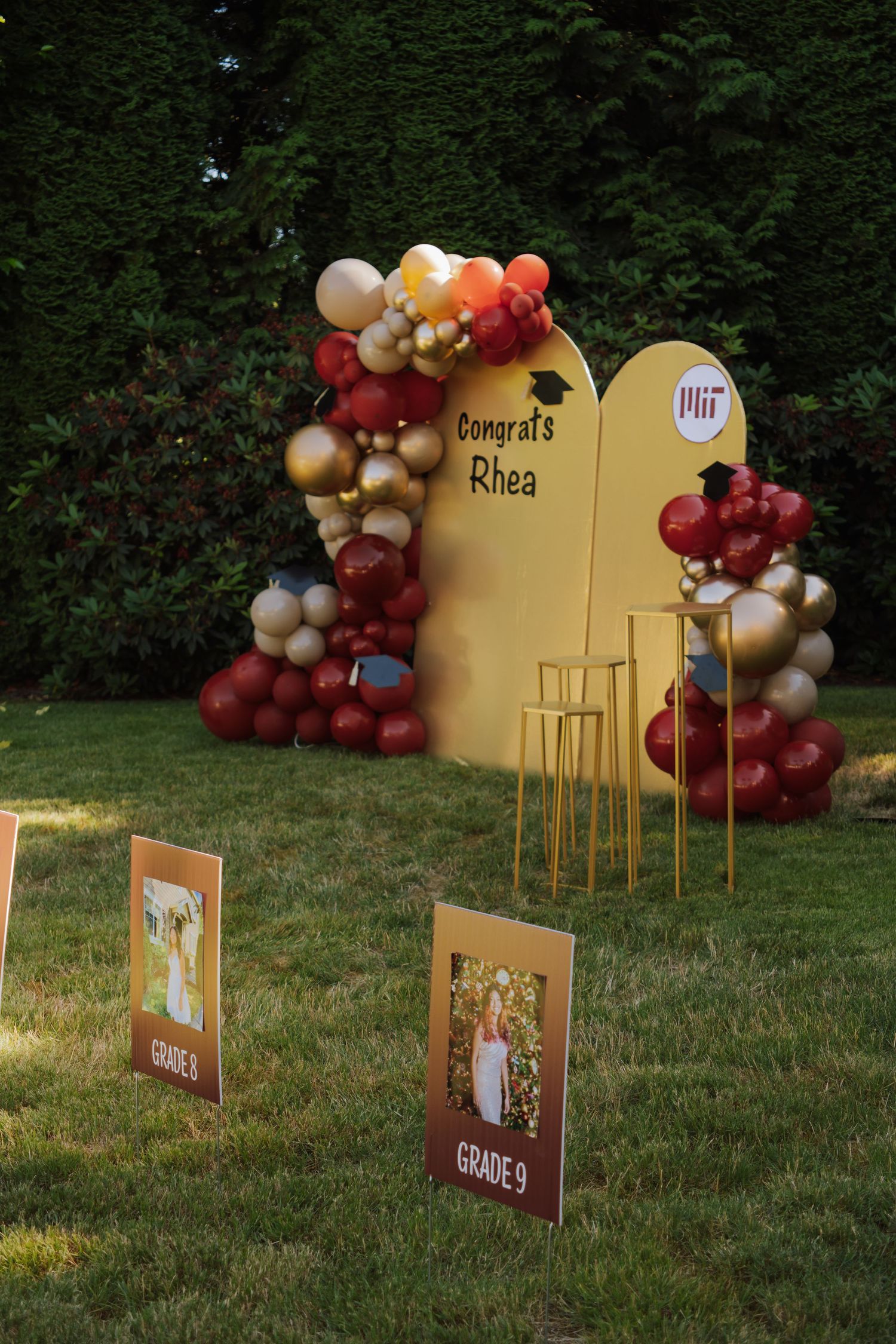 Outdoor graduation party display with colorful balloons and Congrats Rhea MIT sign.