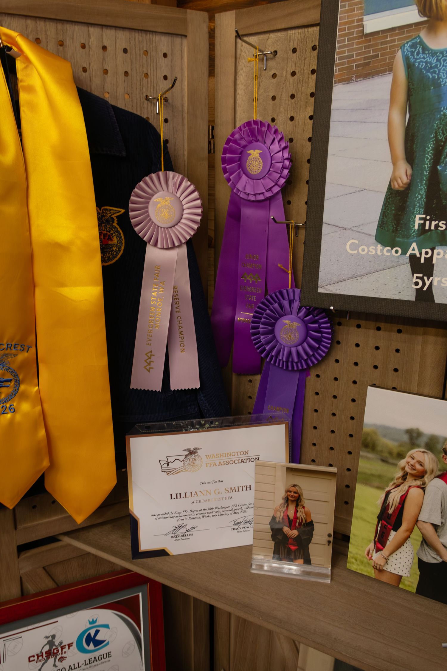 Close-up of purple FFA competition ribbons, graduation stole, certificates, and photos on display shelf.