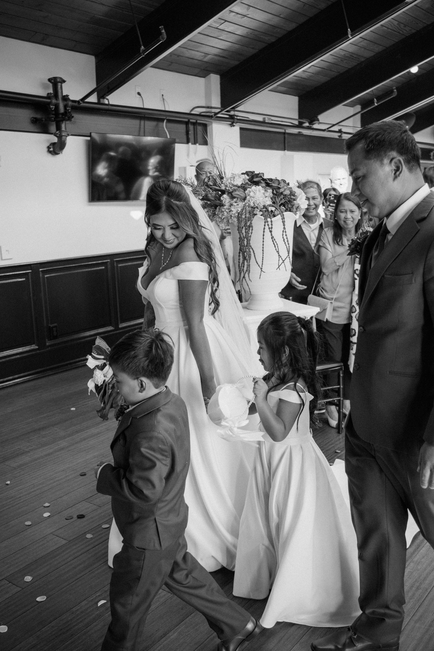 Black and white photo of bride and groom with flower girl and ring bearer during wedding ceremony.