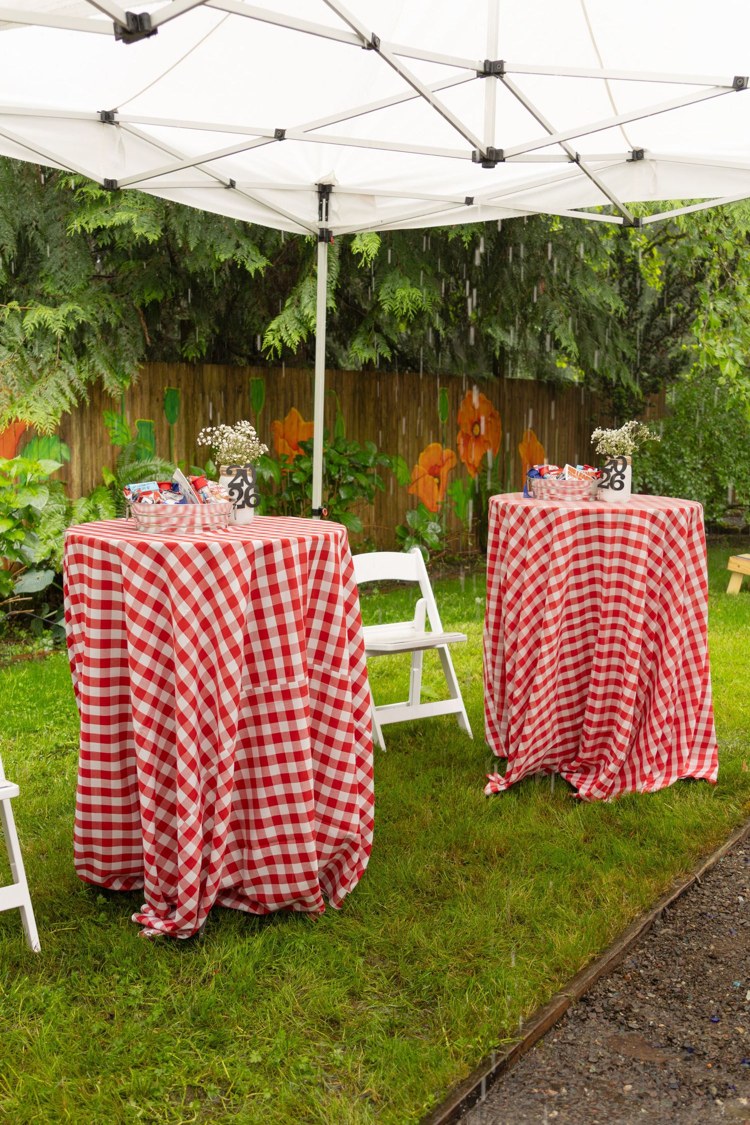 Red and white checkered tablecloths on outdoor tables under white canopy tent.