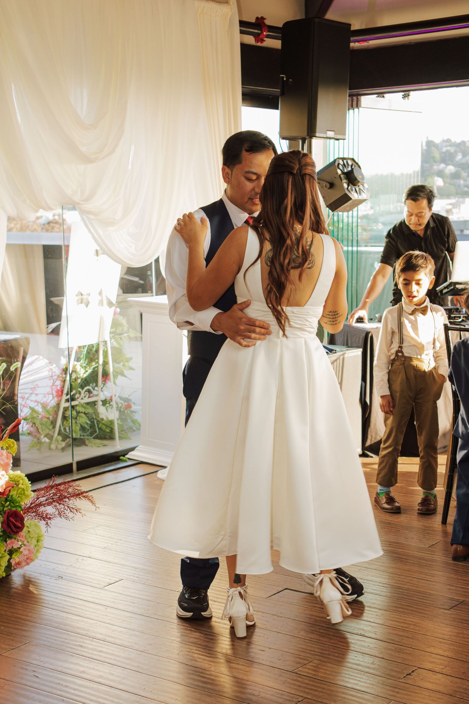 Bride and groom share their first dance at wedding reception with white drape backdrop.