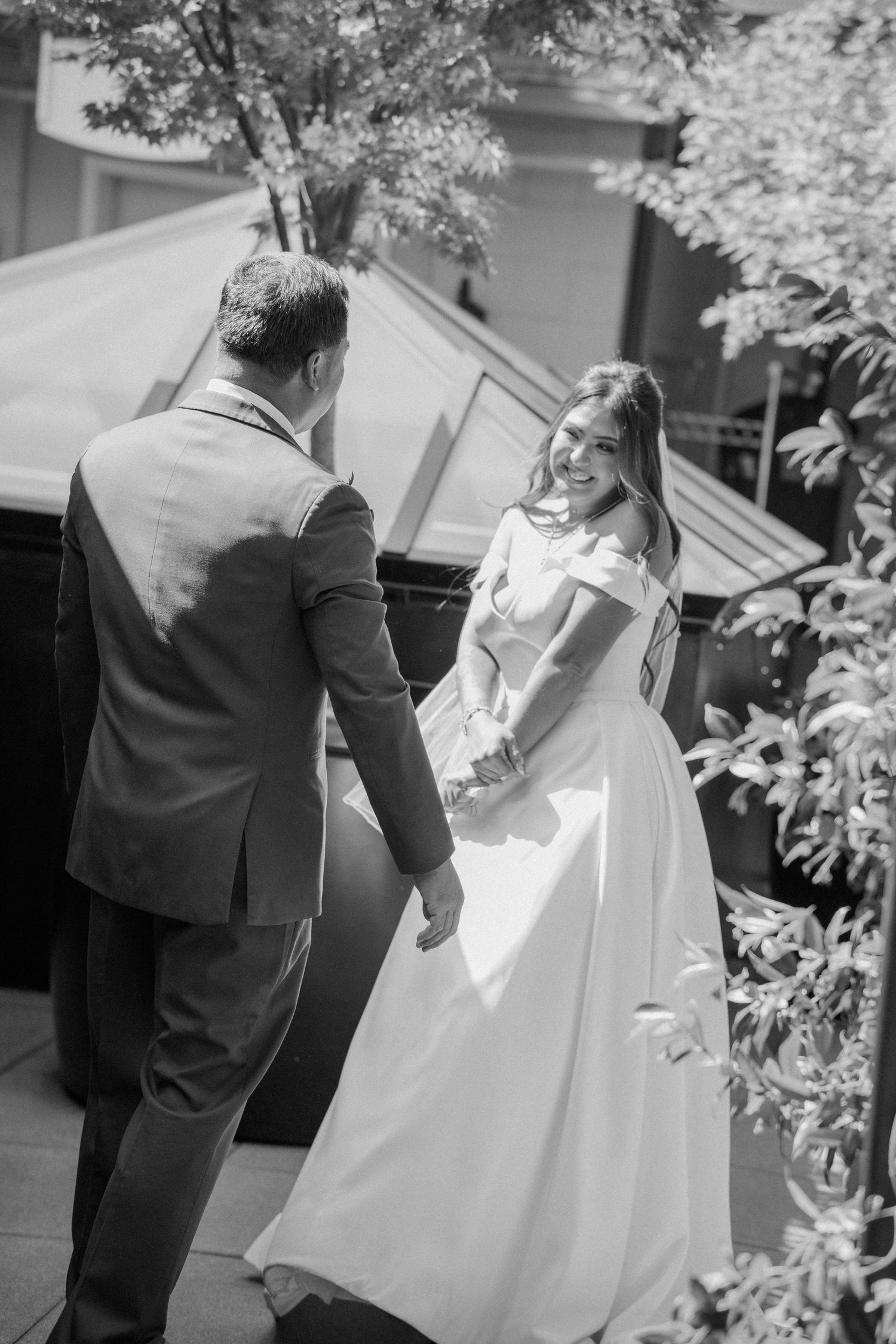 Black and white photo of bride smiling at groom during outdoor first look reveal.