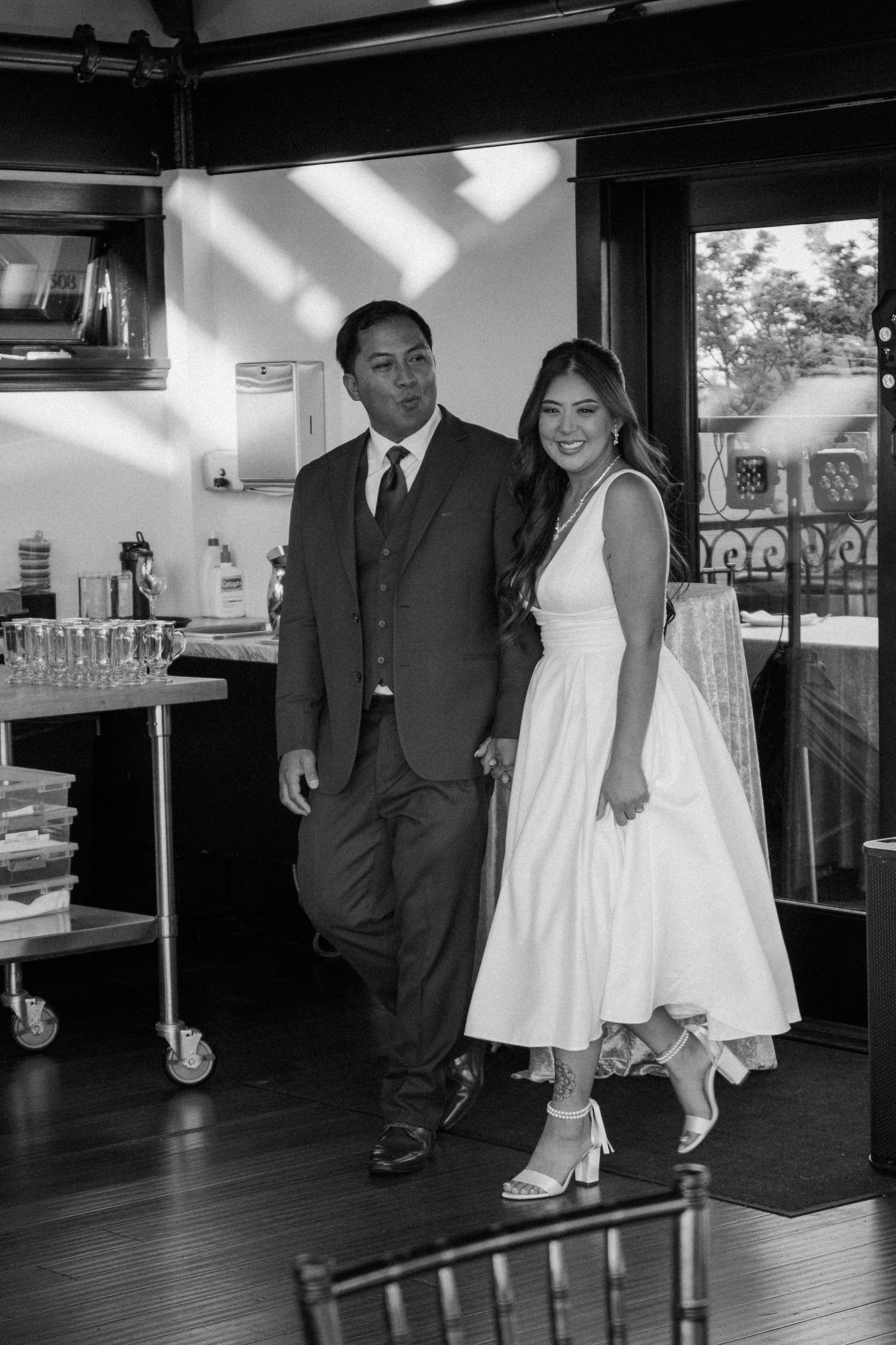 Black and white photo of couple in wedding attire smiling together inside a reception venue.
