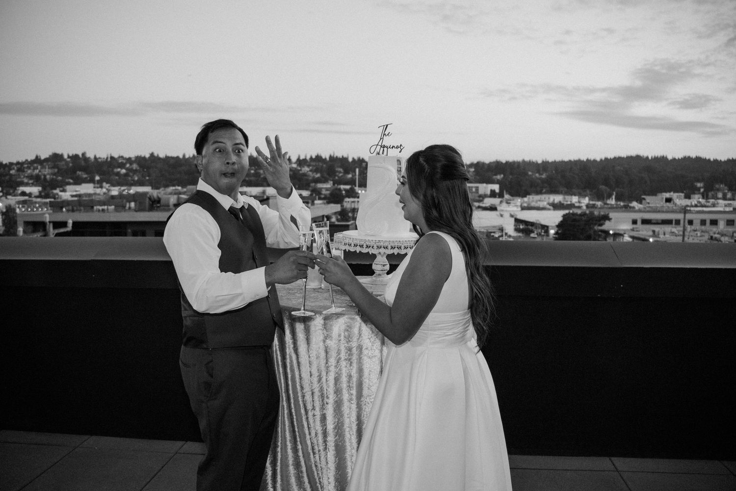 Bride and groom cut wedding cake on rooftop at sunset in black and white photo.