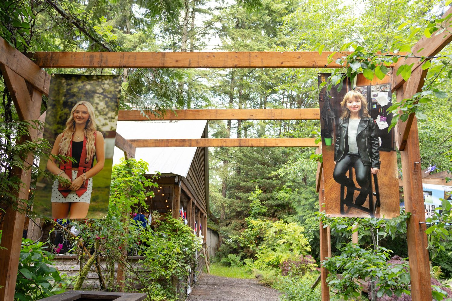 Wooden garden gate entrance with photos displayed among lush green trees and foliage.