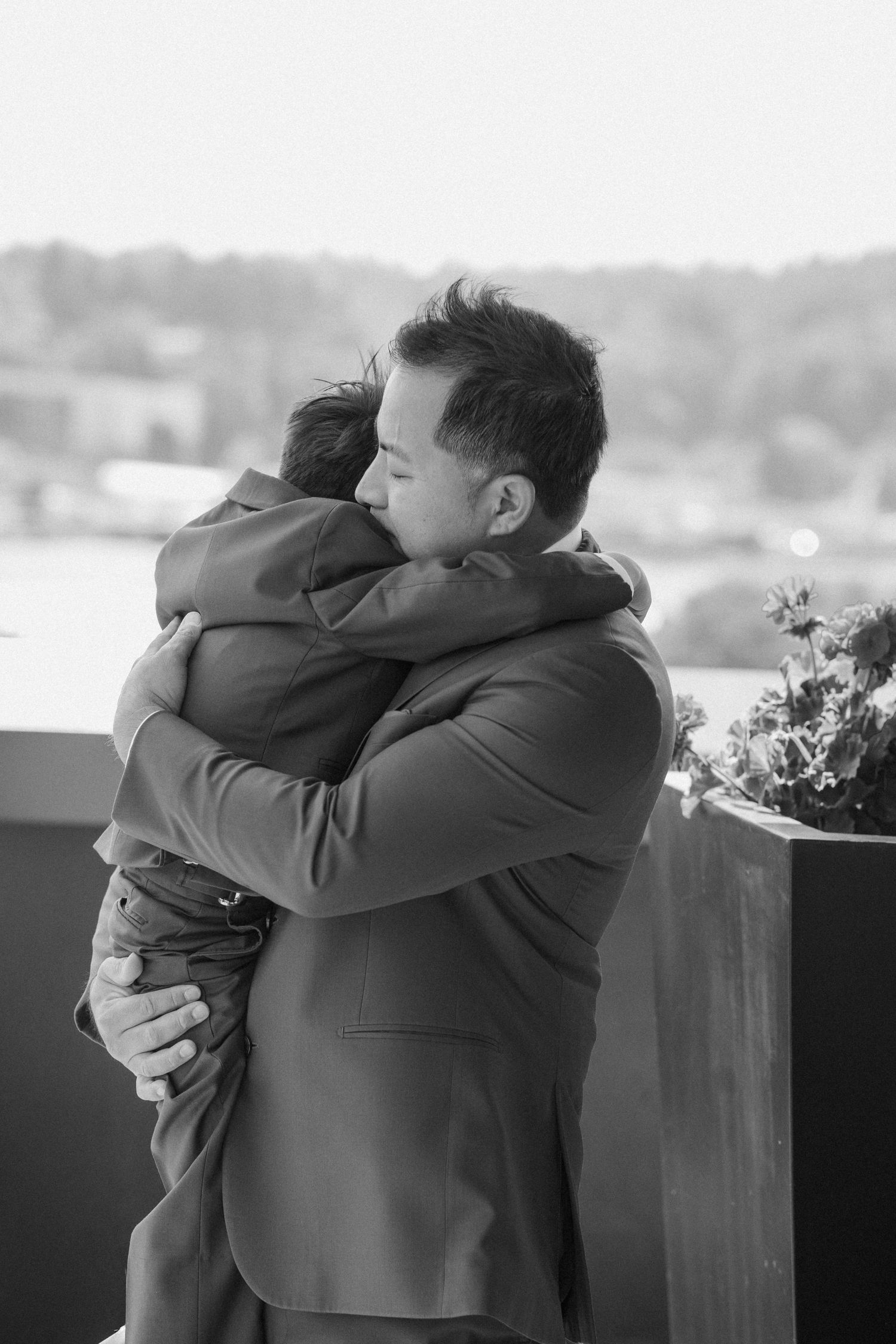 Emotional black and white photo of groom hugging guest on outdoor wedding venue balcony.