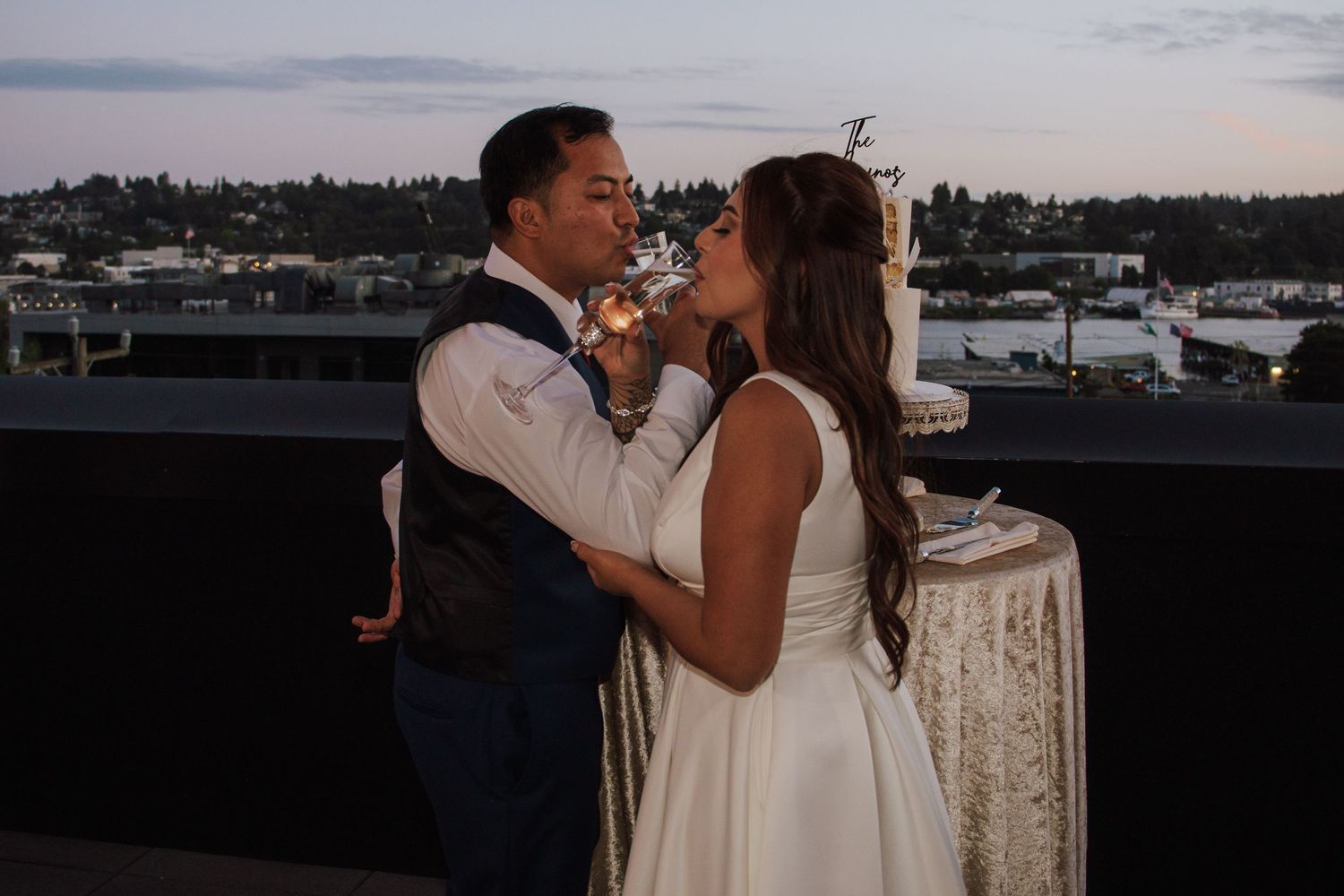 Bride and groom share a kiss on rooftop terrace at twilight after cake cutting ceremony.