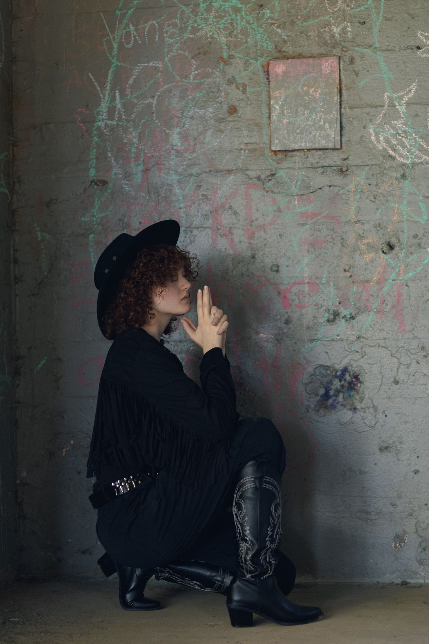 a grunge and all black dressed cowgirl poses in brutalist concrete architecture  for this blend of old and new in a portrait photoshoot.