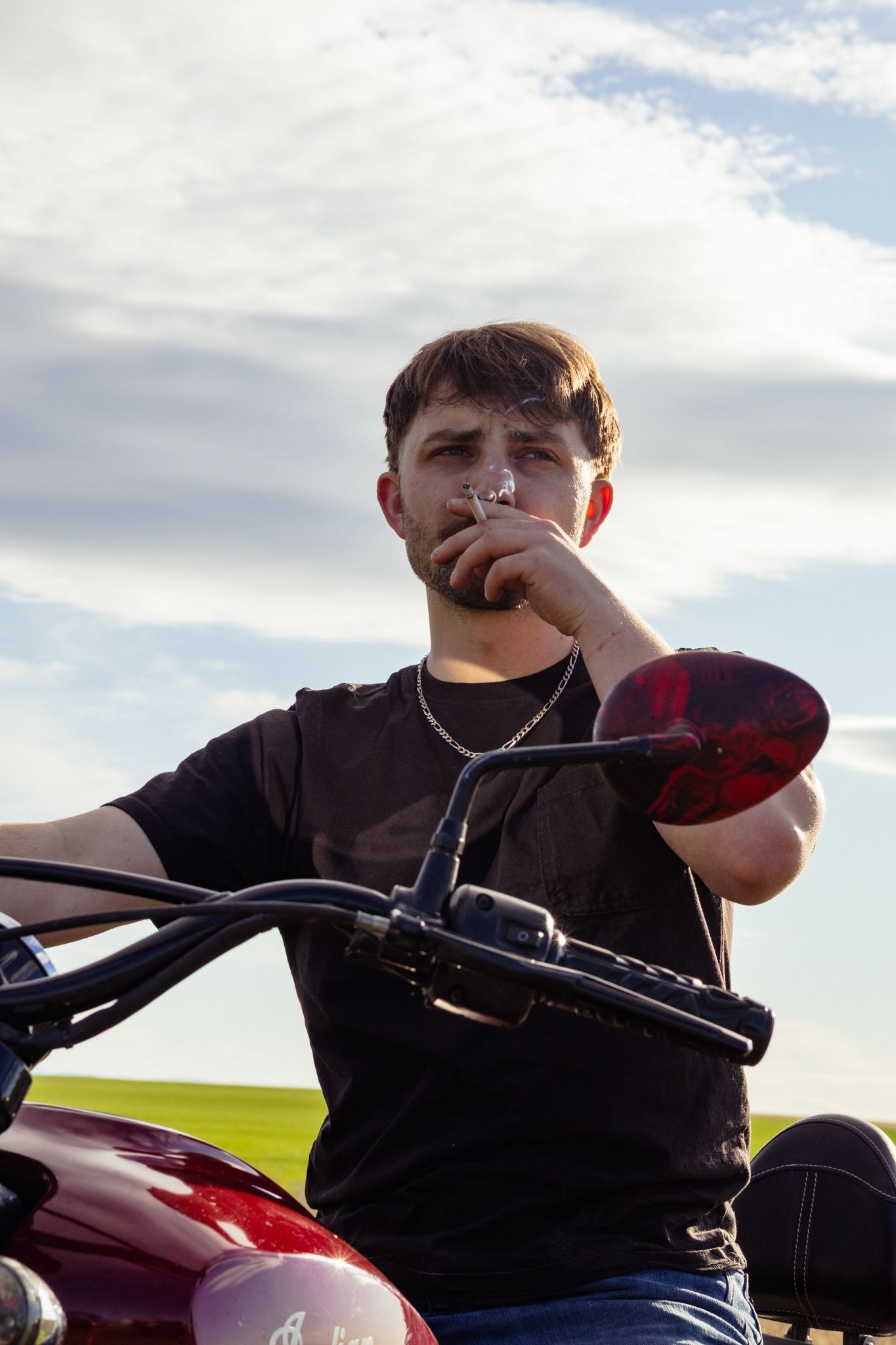 A young man sits smoking a cigarette while looking out over his Indian motorcycle.