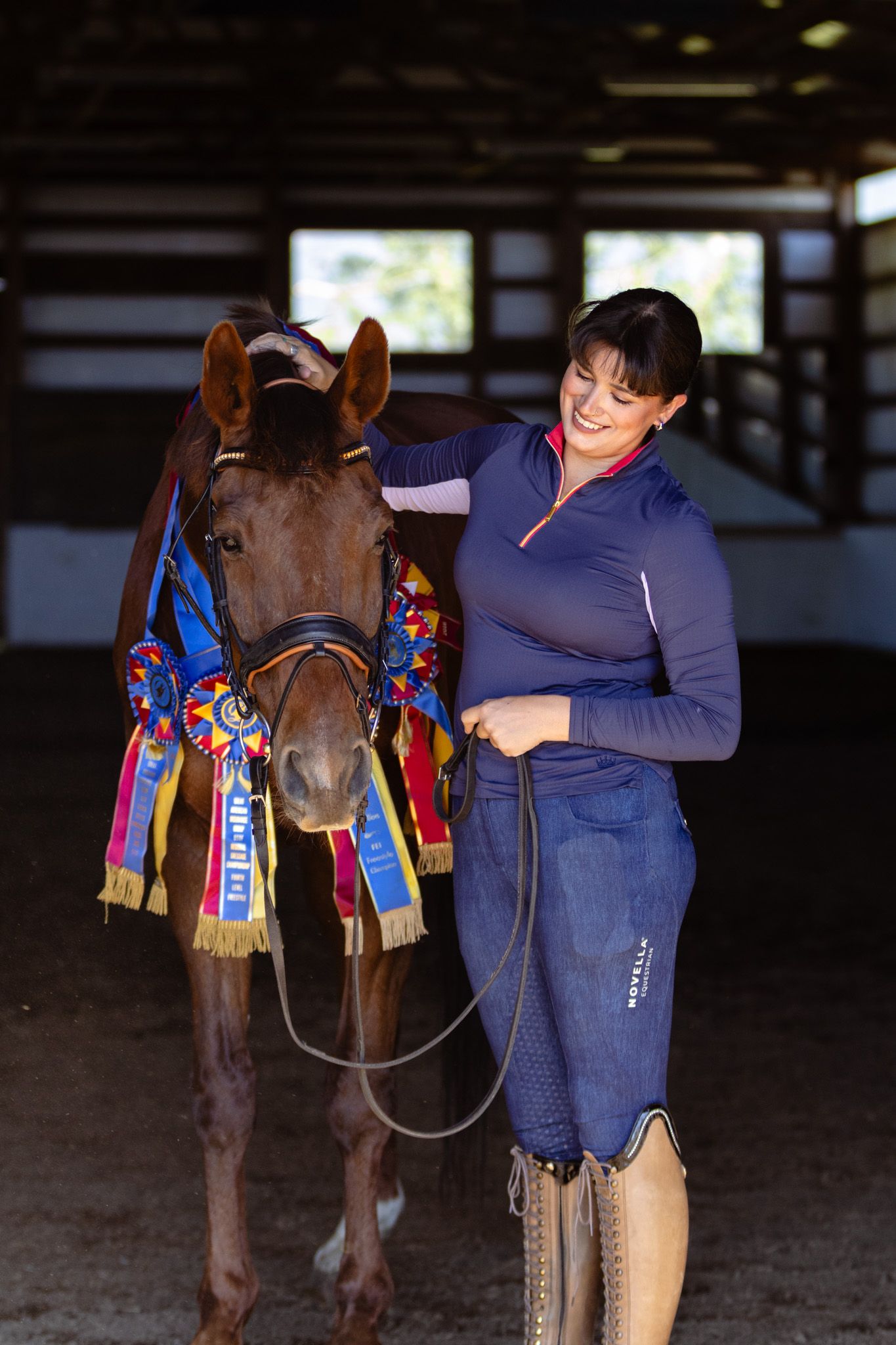 A dressage rider poses with her horse and their many big ribbons together.
