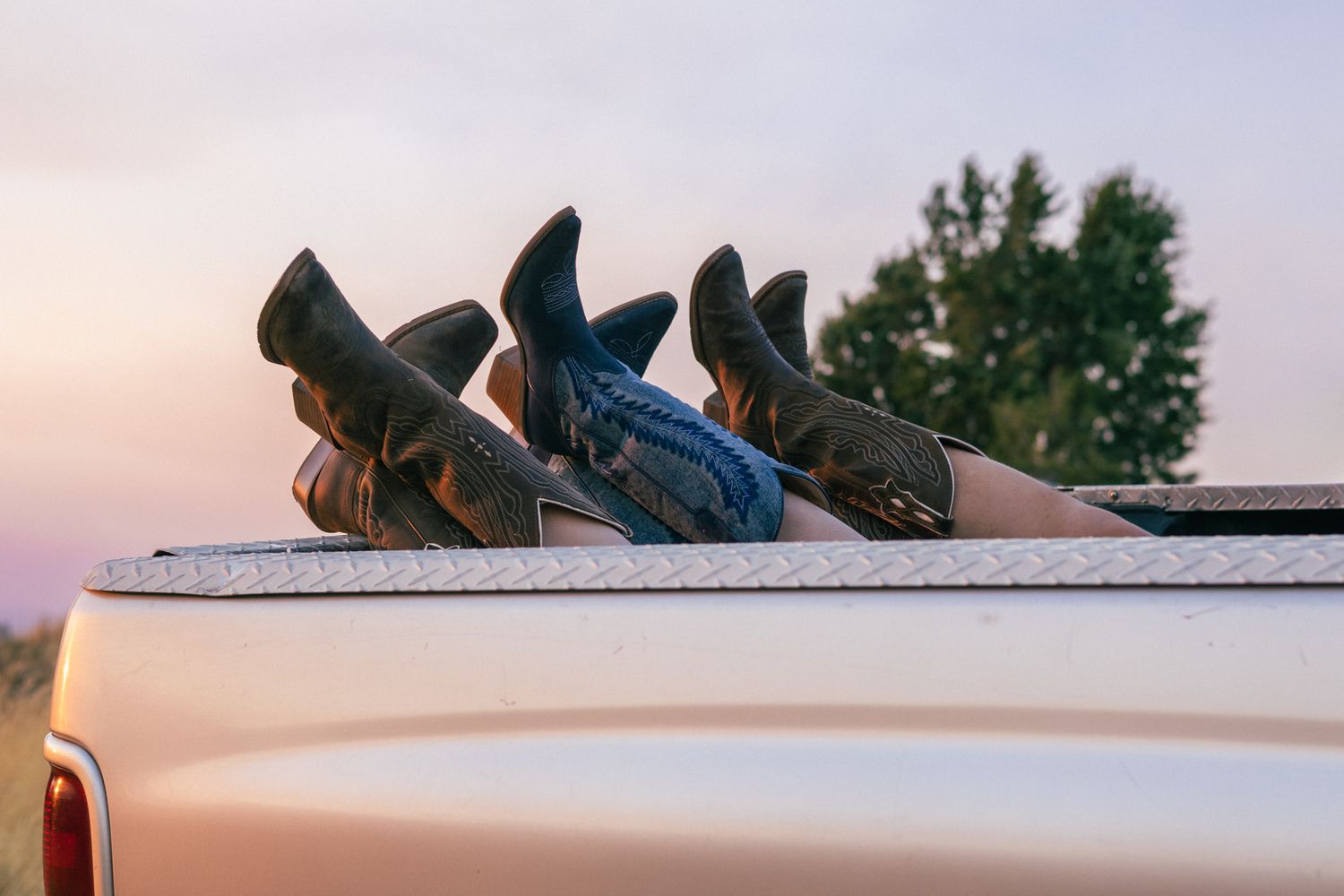 three pairs of boots are crossed in the bed of a truck watching the sunset.