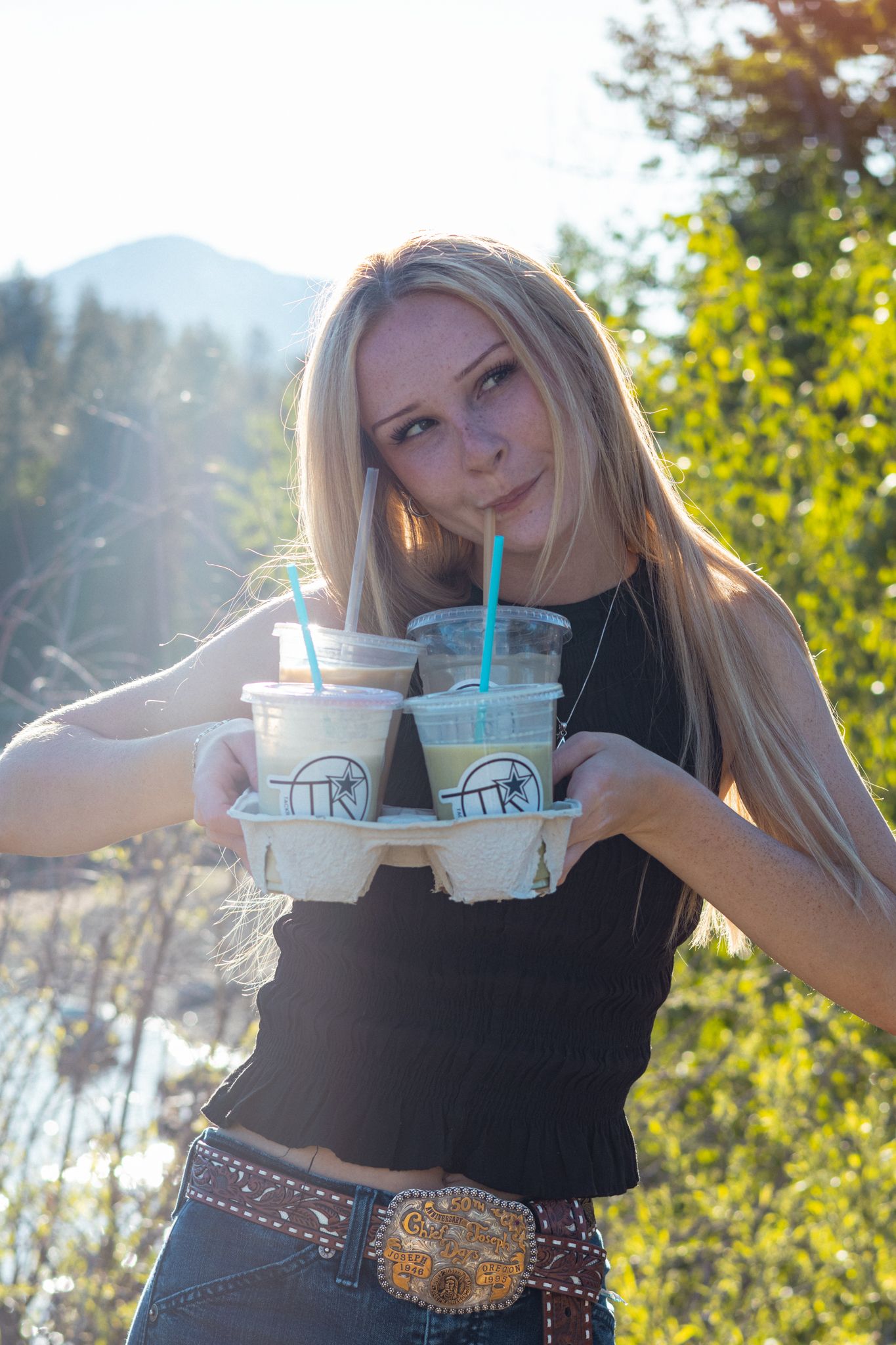 A blonde woman smiles while drinking from a tray of coffee products.
