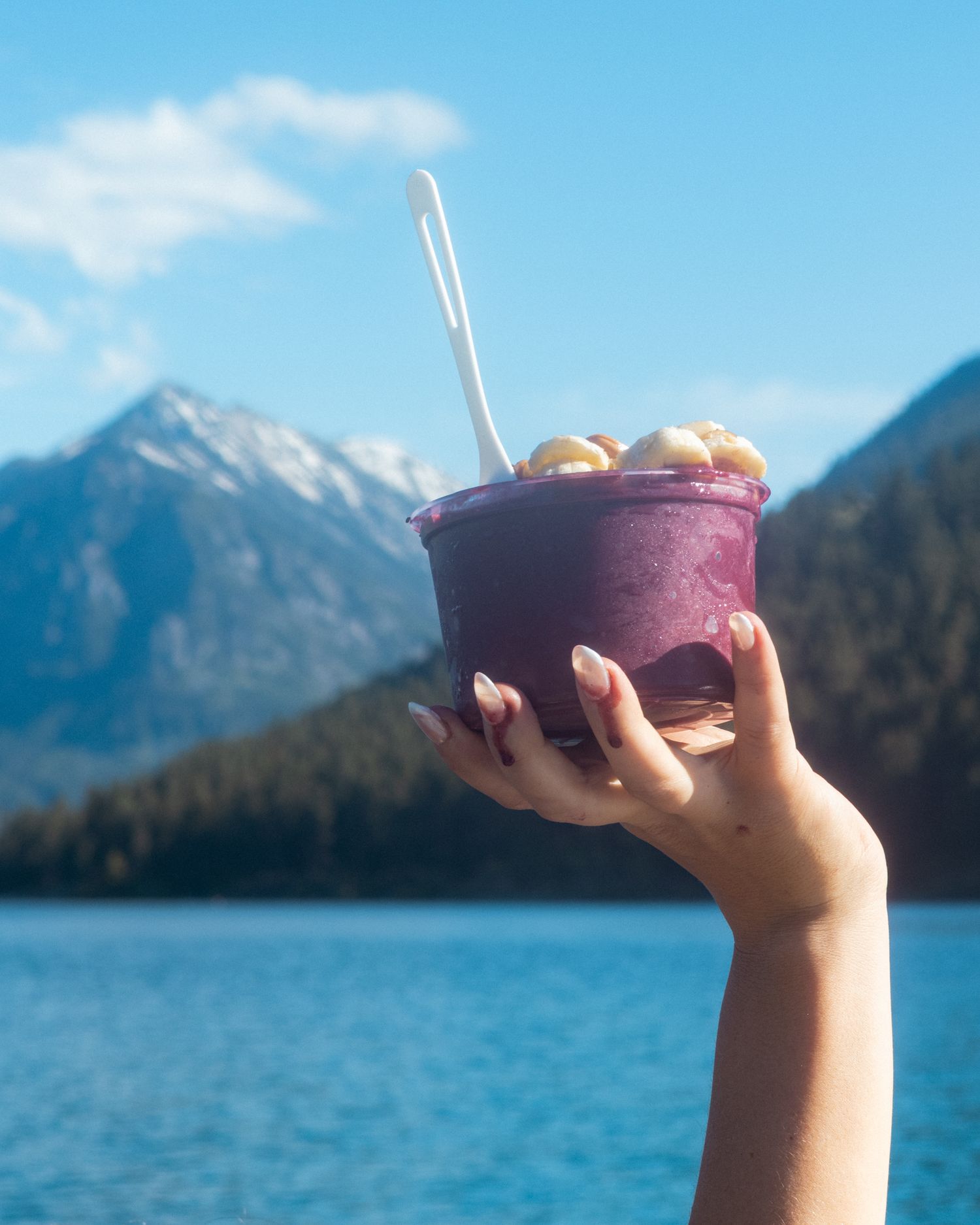 An Açai bowl photographed dripping over a woman's fingers with mountains in the background.