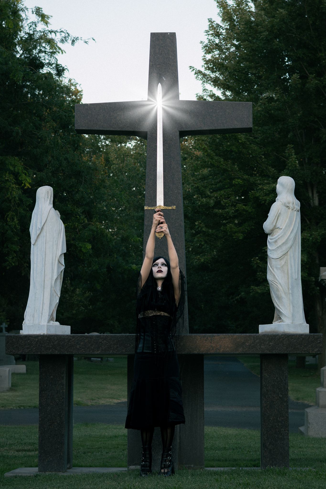 Girl lifts a glittering sword at this gothic styled cemetery photoshoot.