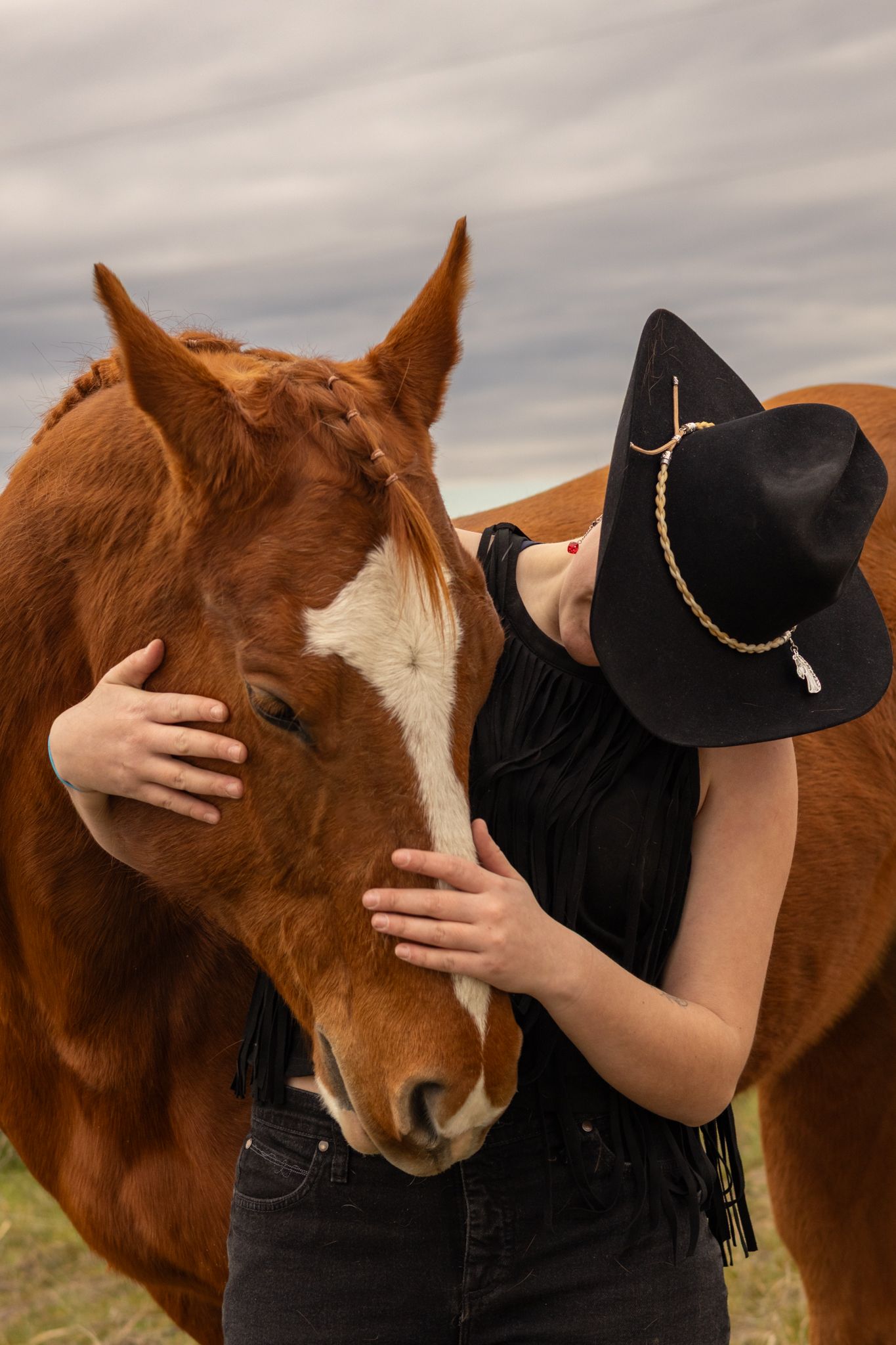 A cowgirl hides her face as she holds her horses head in this senior portrait session in Pasco.