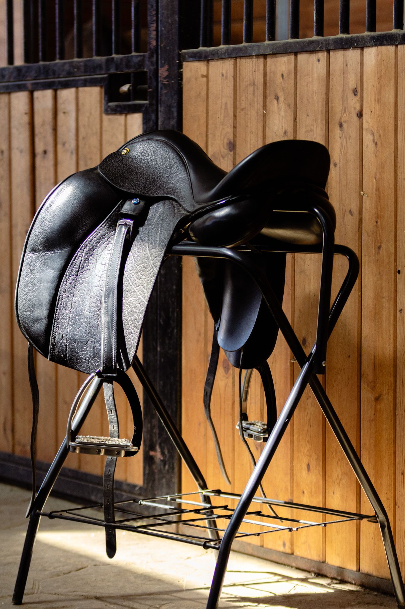A beautiful black saddle stands in a stable alleyway for this product photoshoot.
