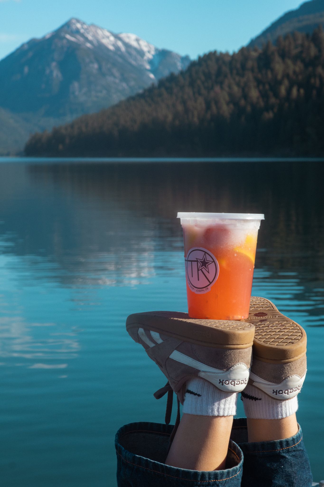 A lemonade sits on a pair of shoes overlooking Wallowa Lake for this coffee branding photoshoot.