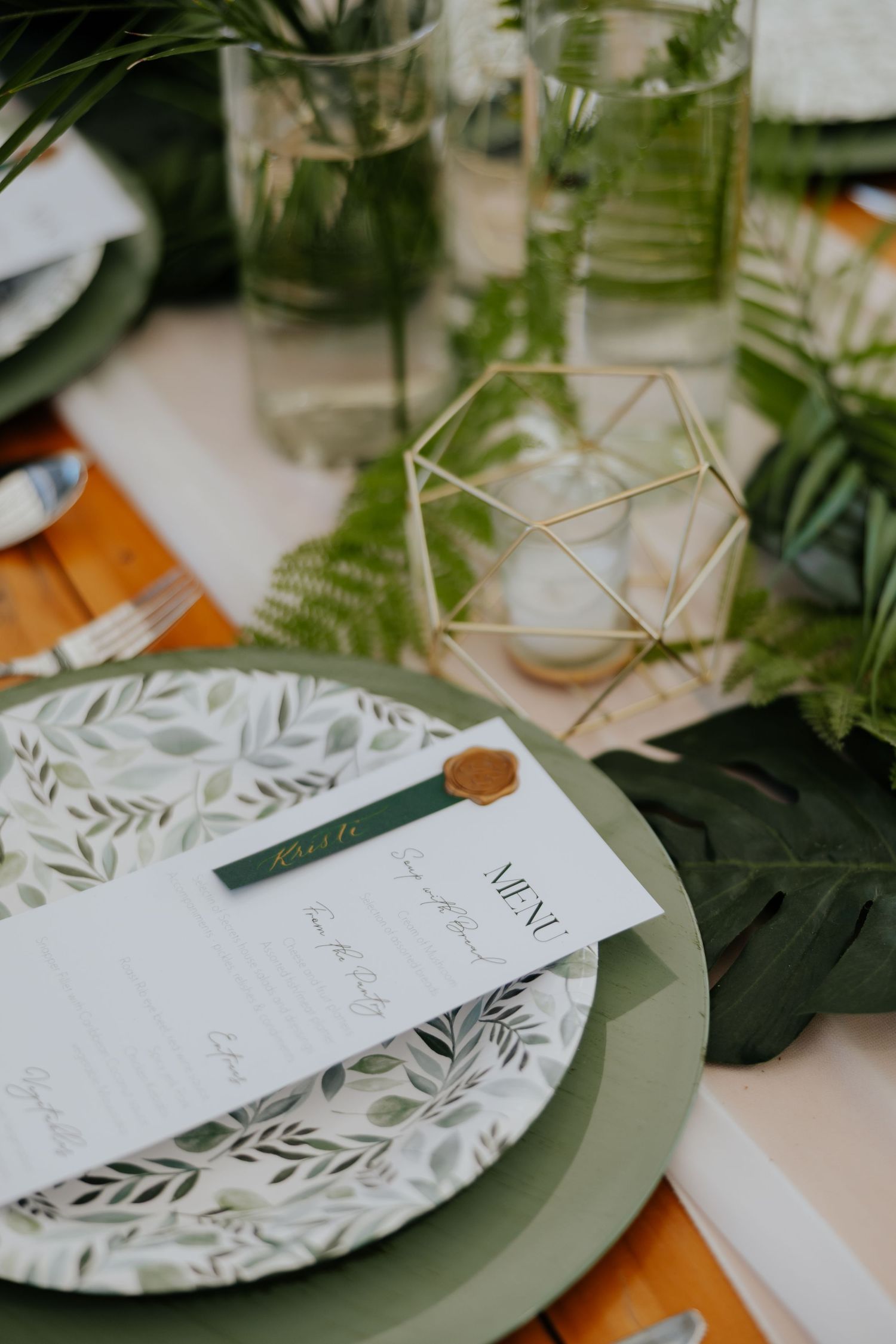 Wedding table setting with botanical plate, menu card, gold wax seal, and geometric gold decor.