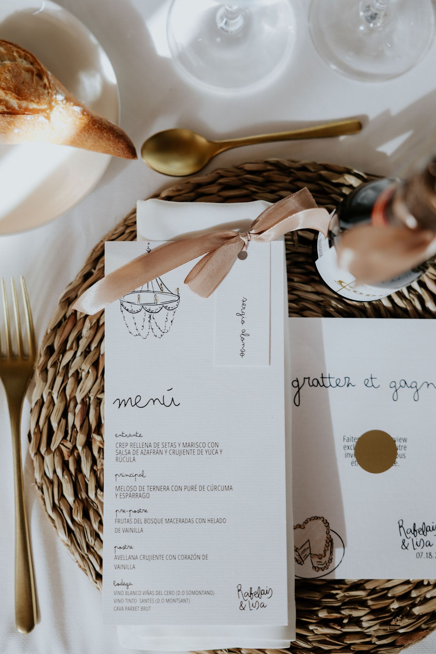 Wedding menu card with ribbon bow displayed on woven placemat with gold cutlery.
