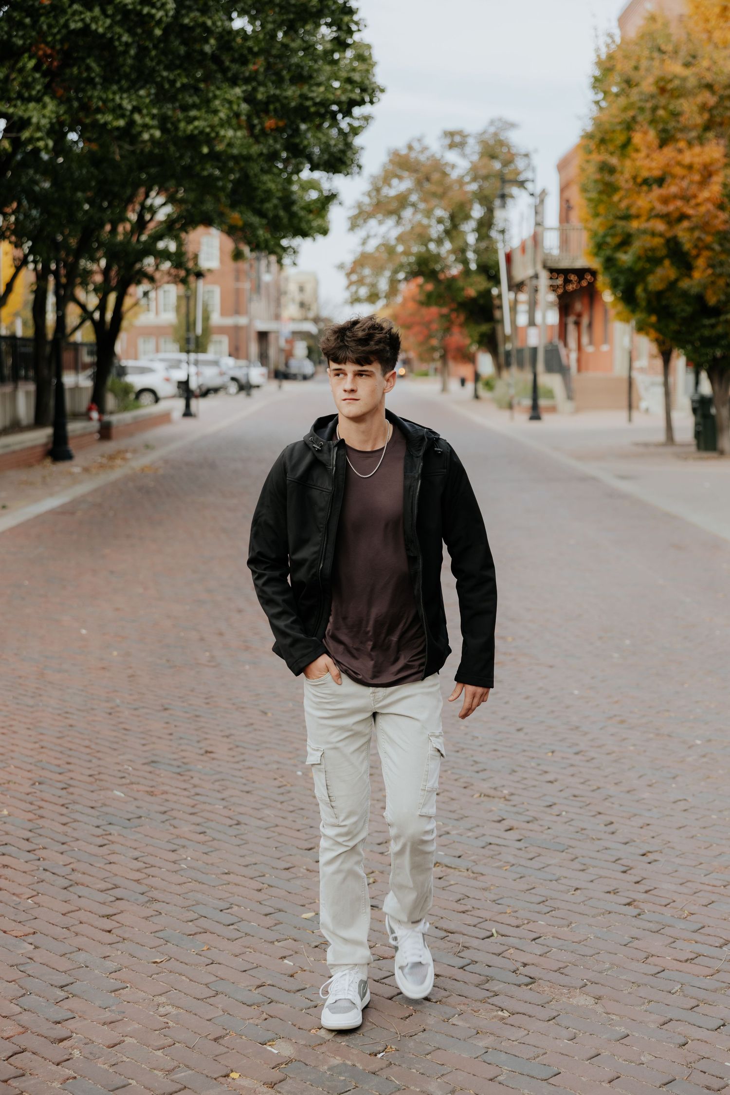 Young man in black jacket and cargo pants walking on brick street in autumn.