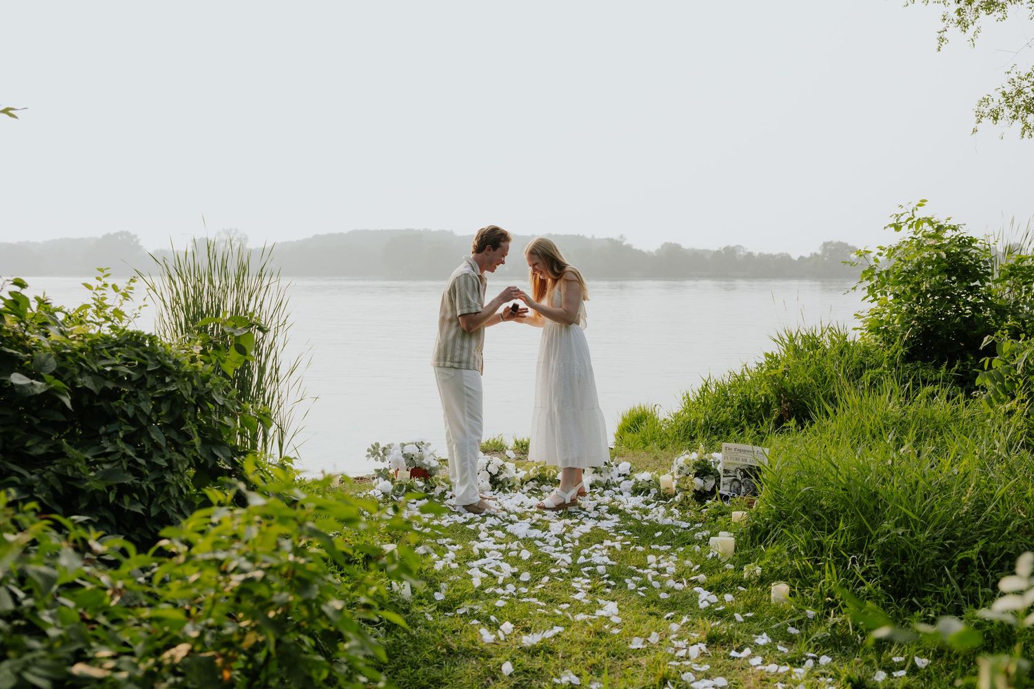 Couple holding hands and sharing a tender moment by a serene lake surrounded by lush greenery.