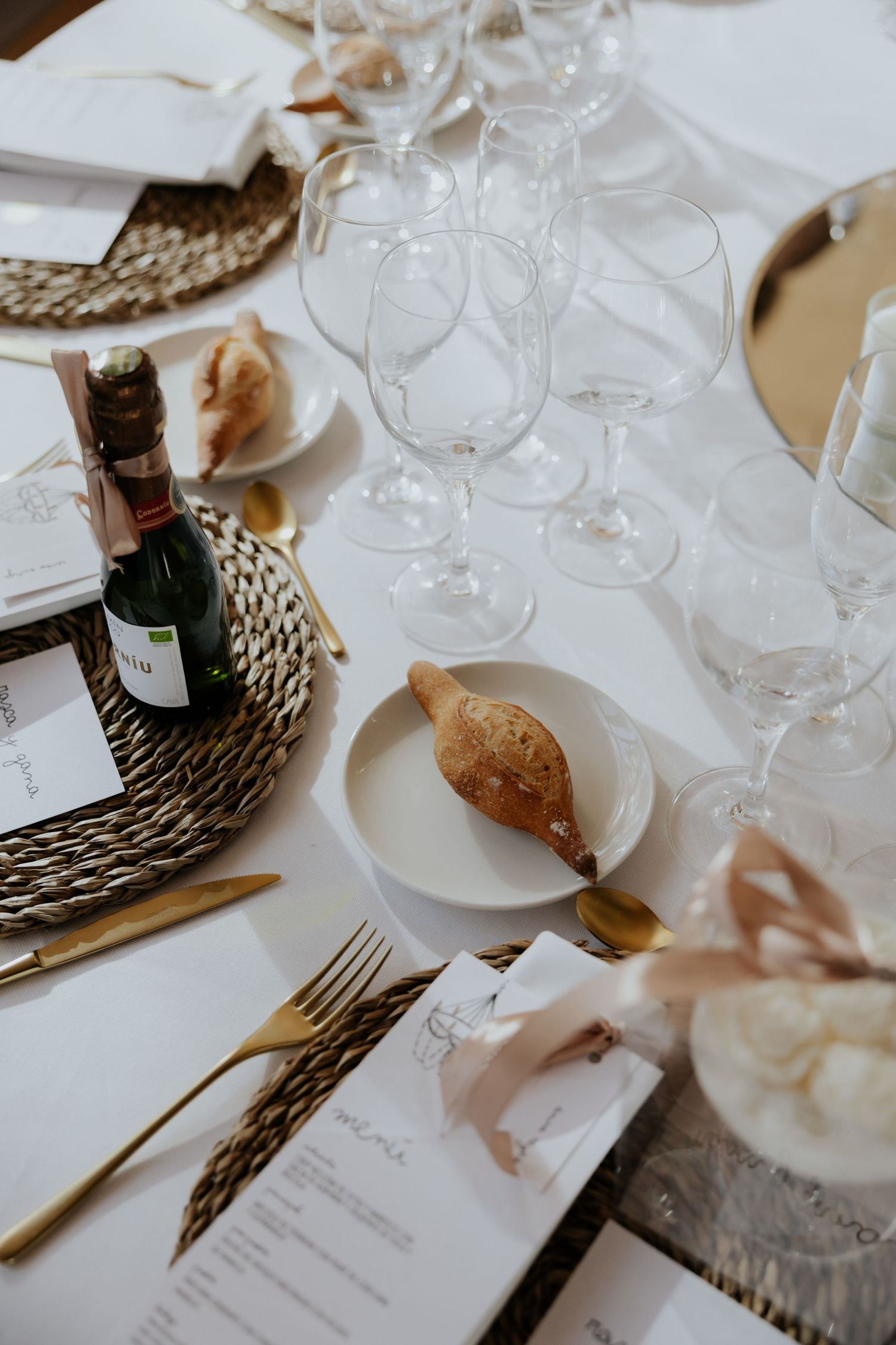 Elegant wedding reception table with gold cutlery, wine glasses, and woven charger plates.
