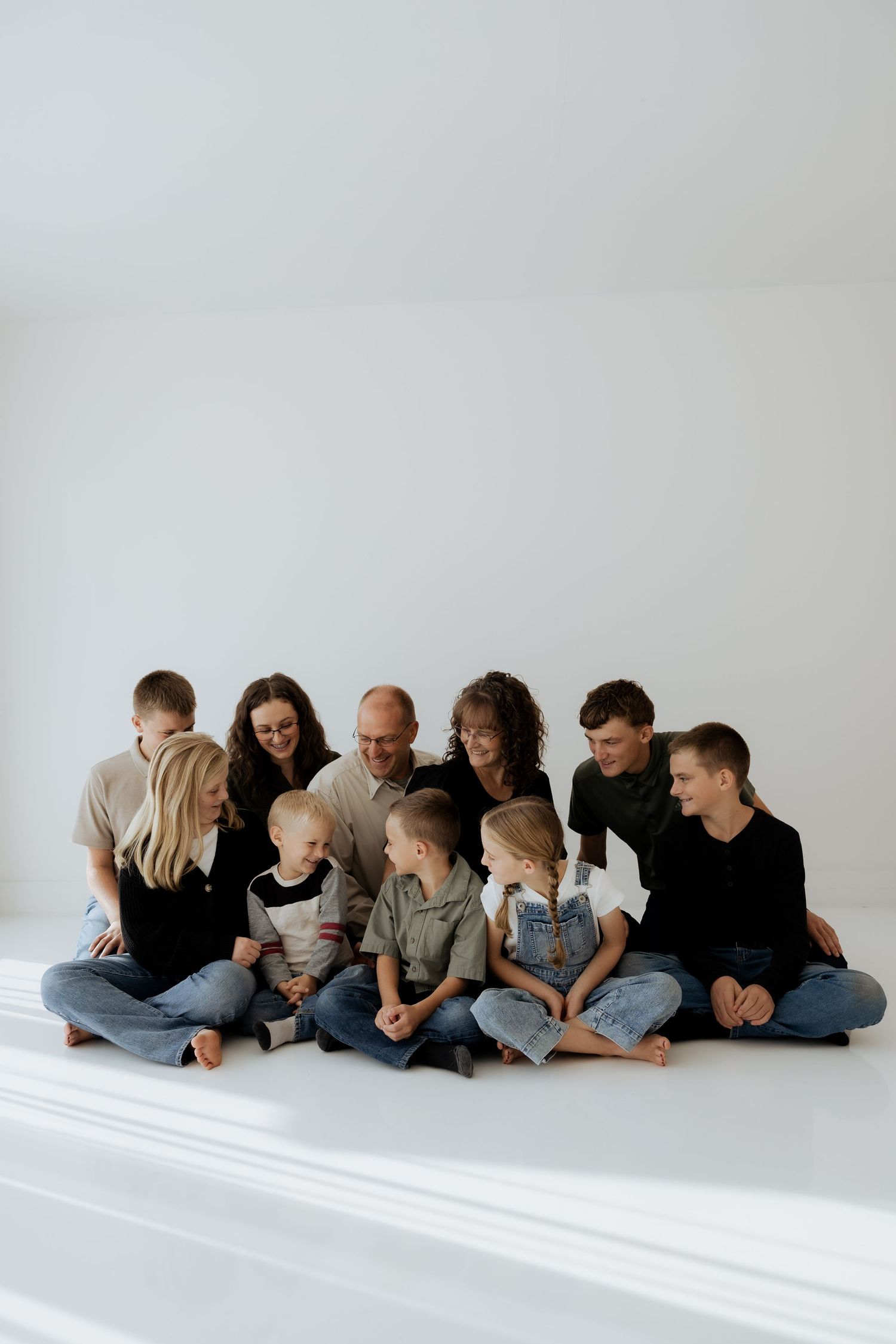 Large family sitting together on white floor in casual black and denim outfits.