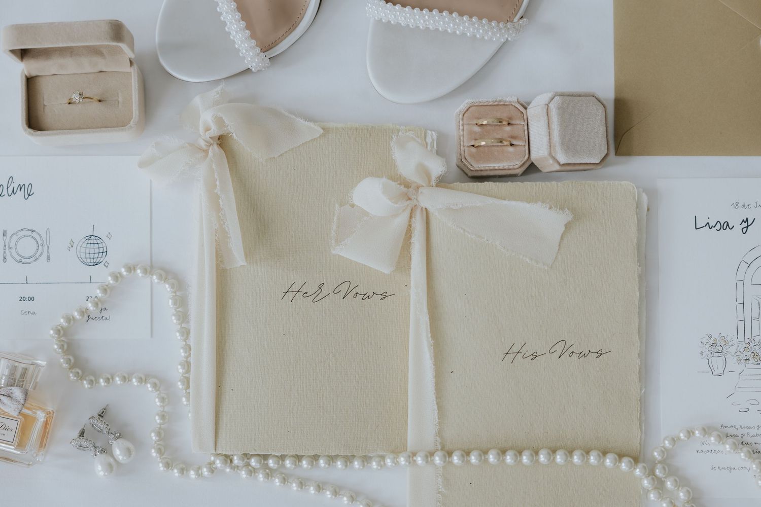 Elegant wedding flat lay with vow books, pearl necklace, rings, and bridal shoes in neutral tones.