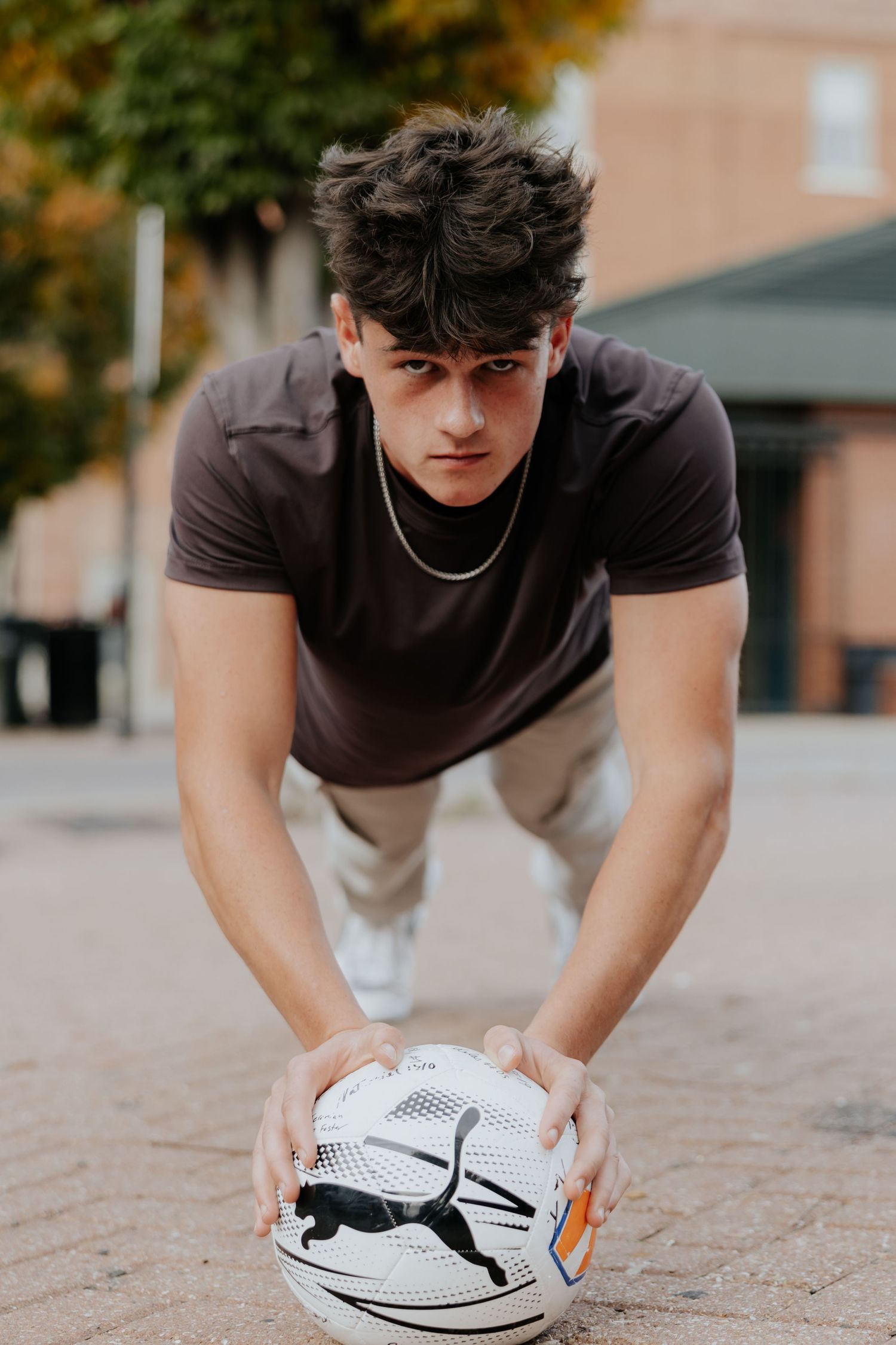 Athletic young man crouching to pick up Puma soccer ball on brick pavement.
