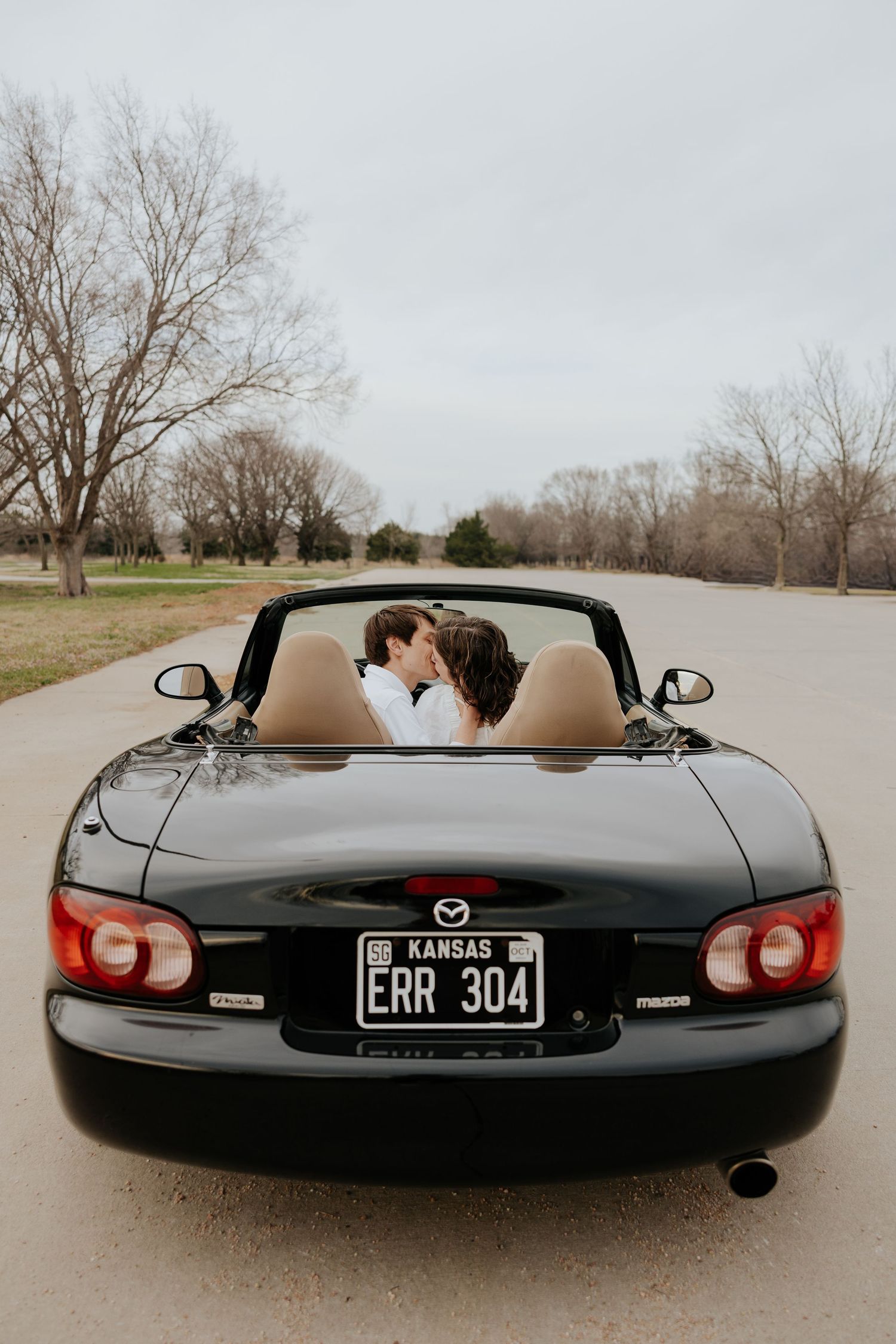 Couple kissing in a black Mazda Miata convertible with Kansas license plate ERR 304.
