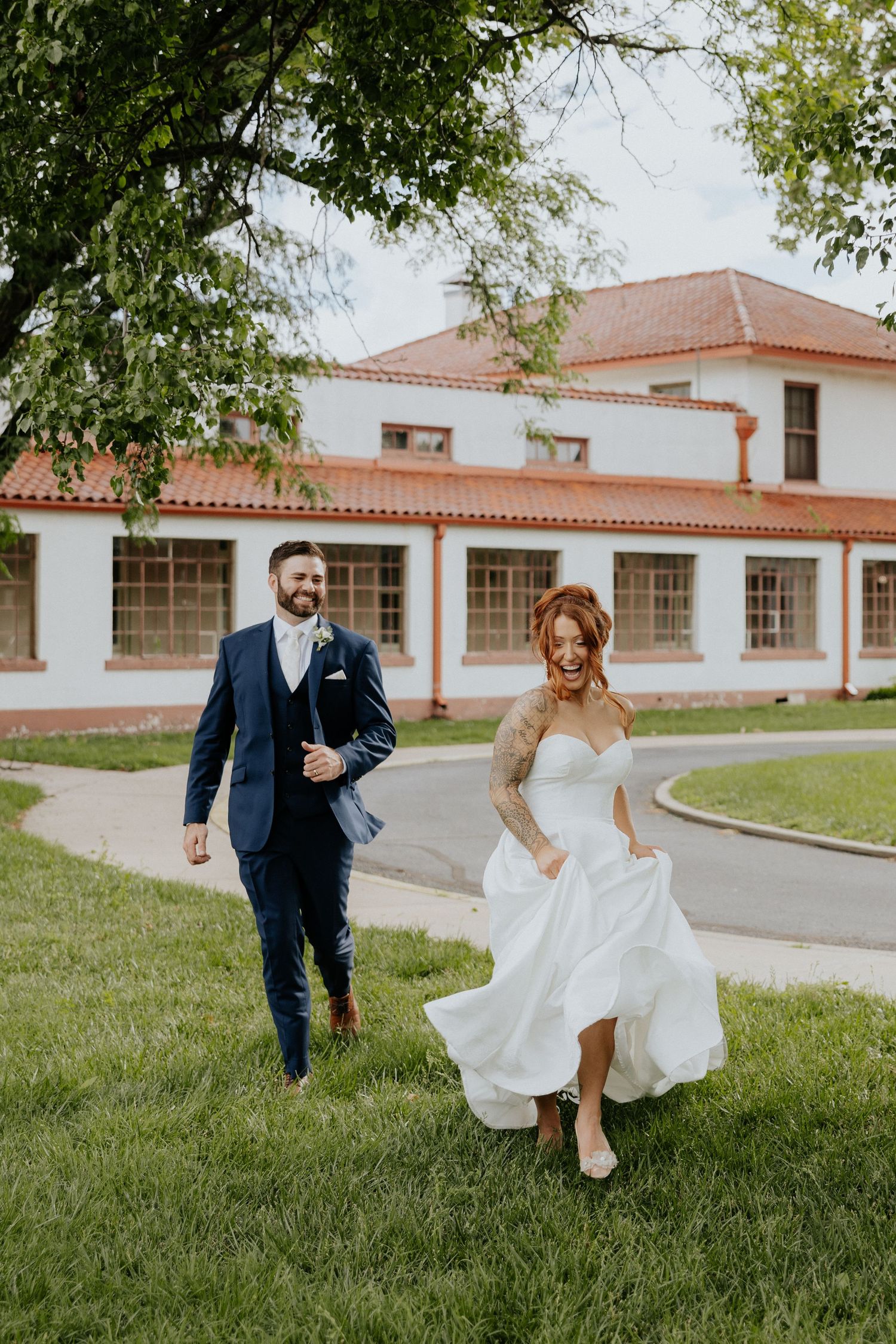 Joyful bride and groom walking together on curved path outside white Spanish-style wedding venue.