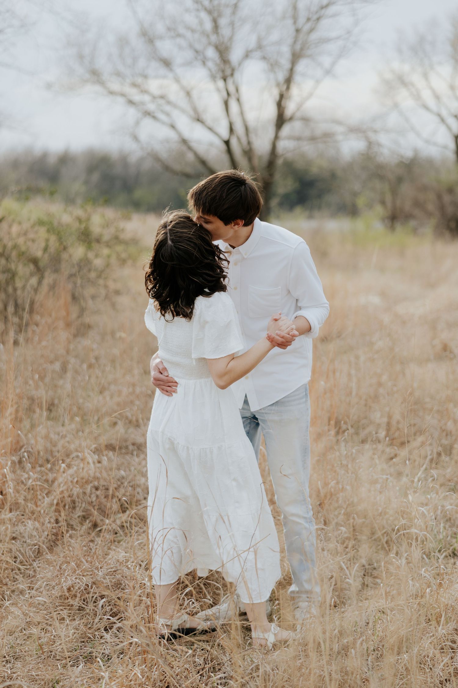 Couple sharing a kiss while embracing in a golden dry grass field outdoors.