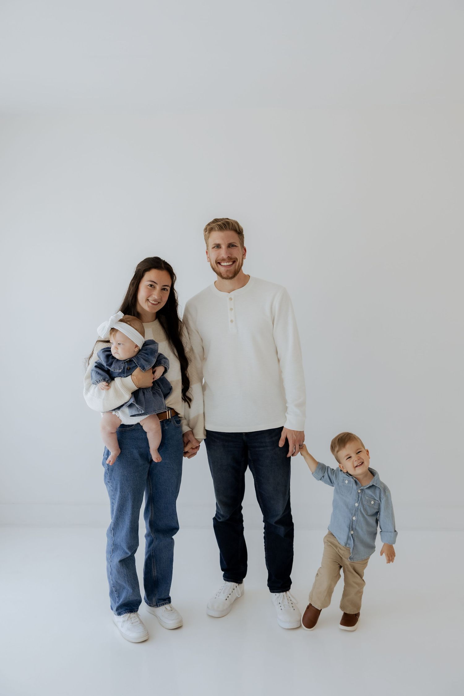 Happy family of four with two young children poses together against a clean white studio background.