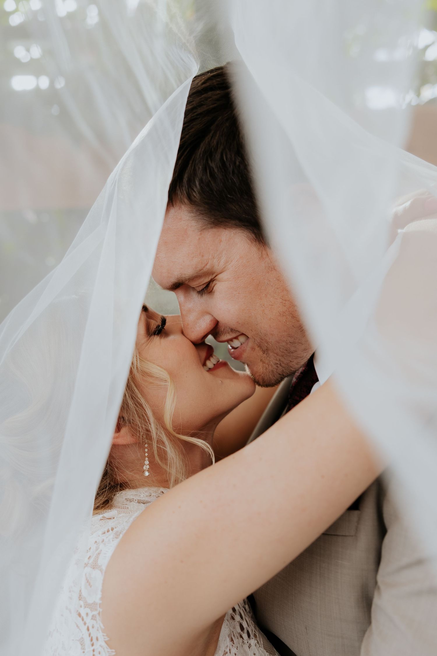 Bride and groom share a romantic kiss beneath a flowing white veil on their wedding day.