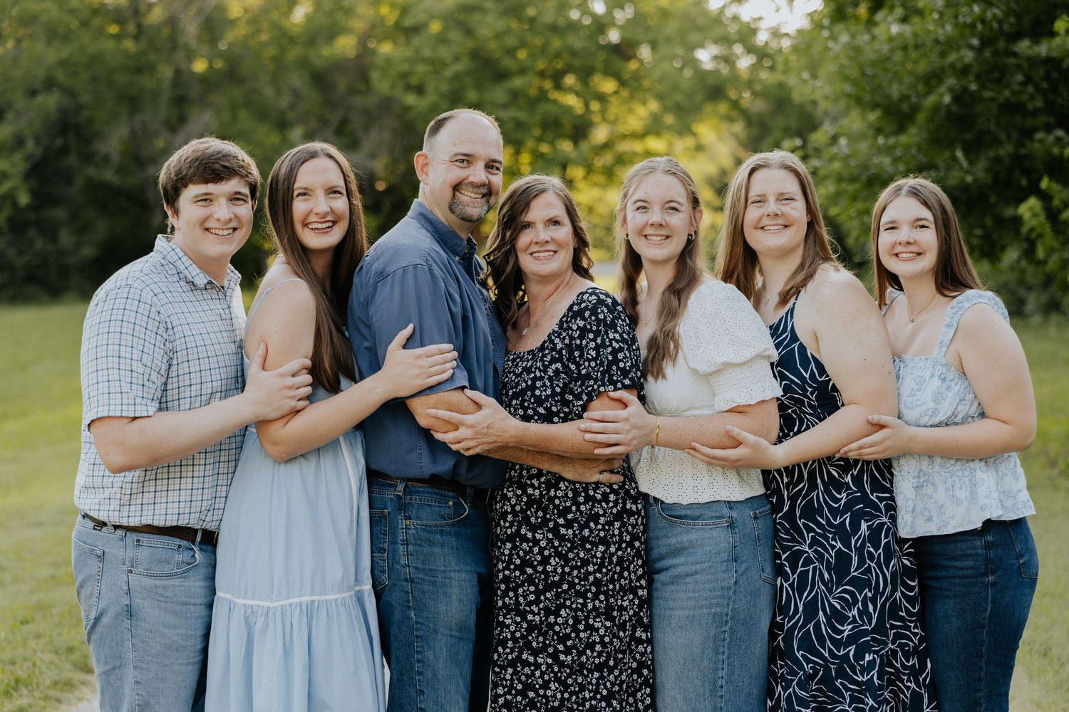 Happy family of seven posing together outdoors in a lush green park setting.