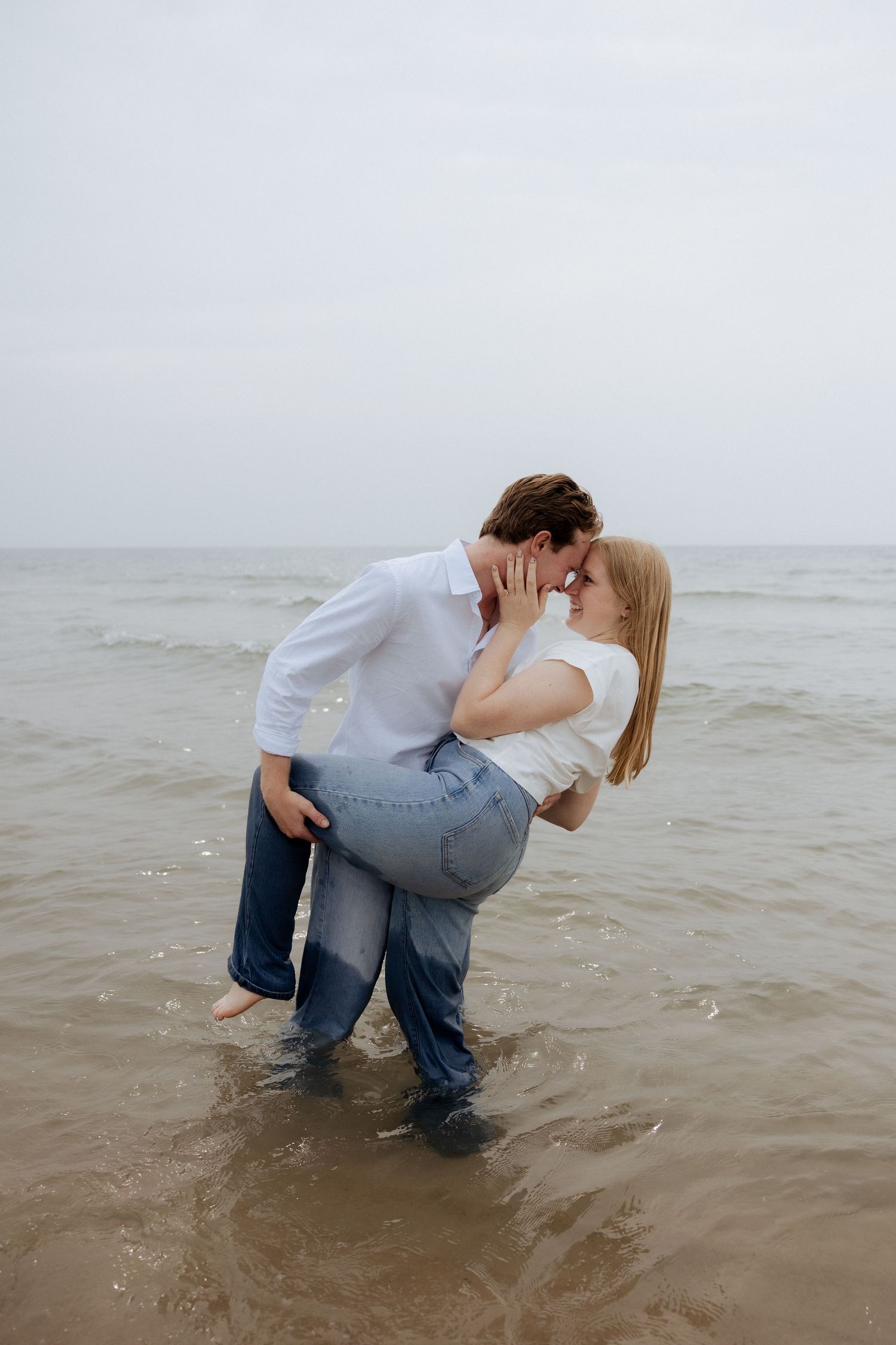 Romantic couple kissing while standing in ocean waves at the beach.