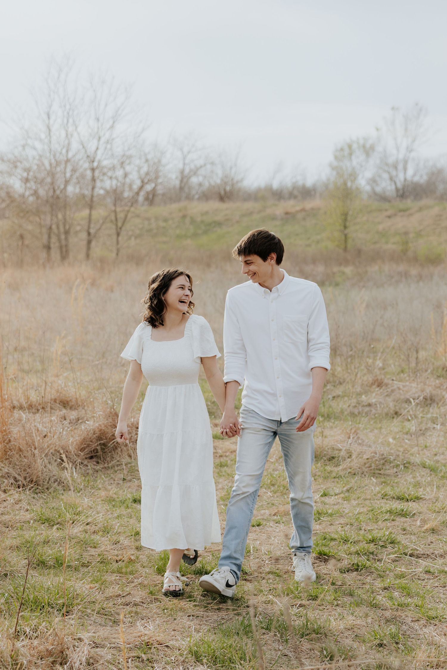 Happy couple laughing and holding hands while walking through a golden meadow.