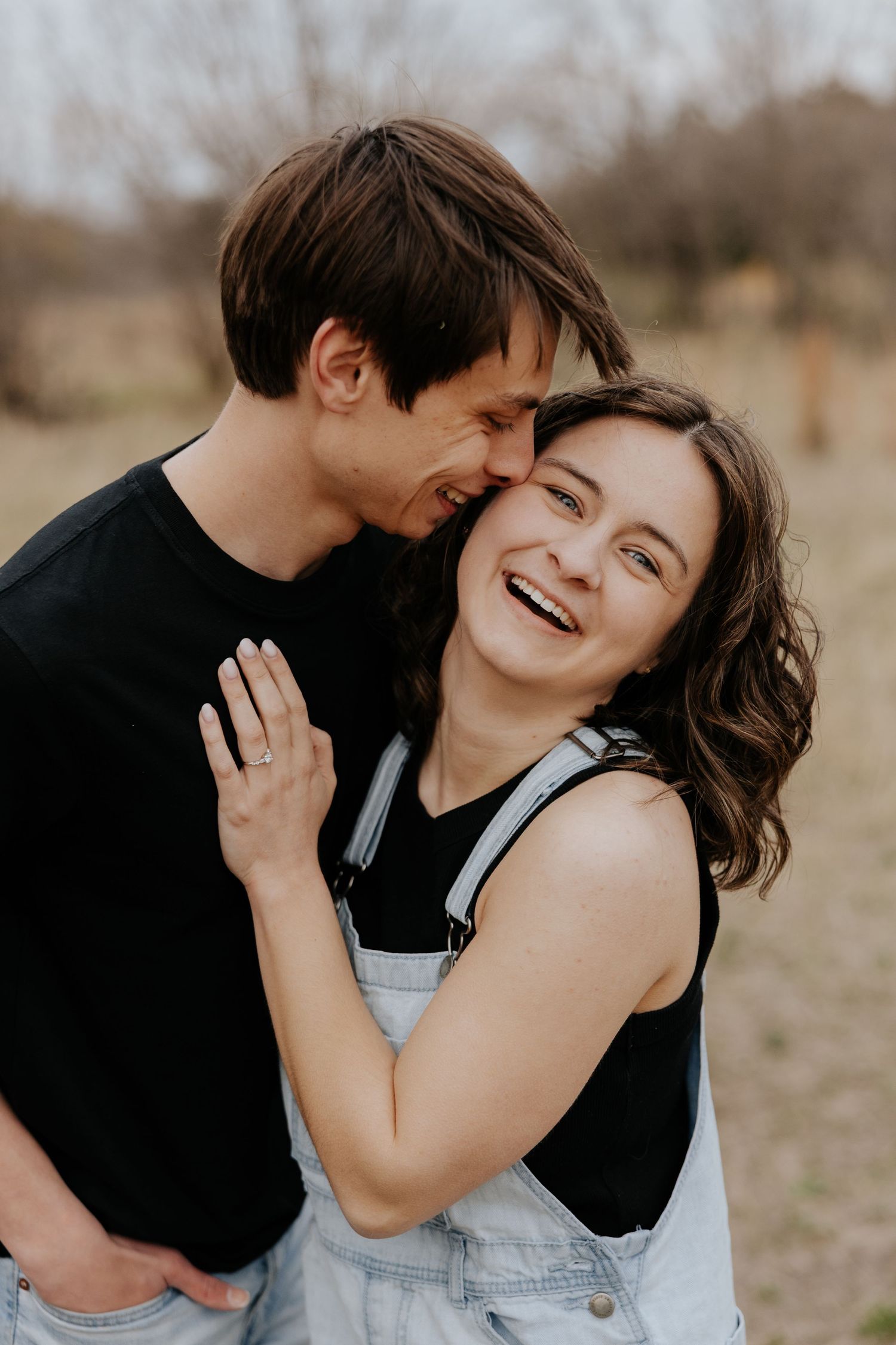 Happy engaged couple laughing and embracing outdoors during a romantic engagement photo session in a field.