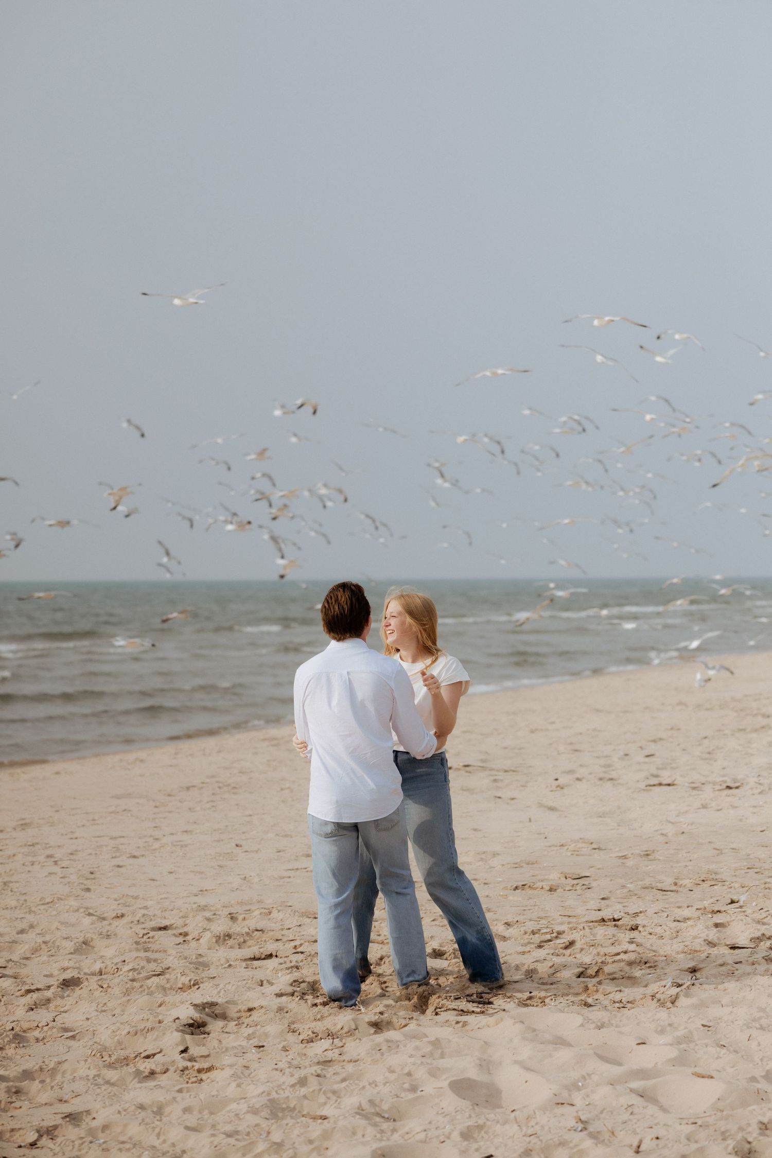 Couple embracing on sandy beach watching seagulls fly over the ocean.