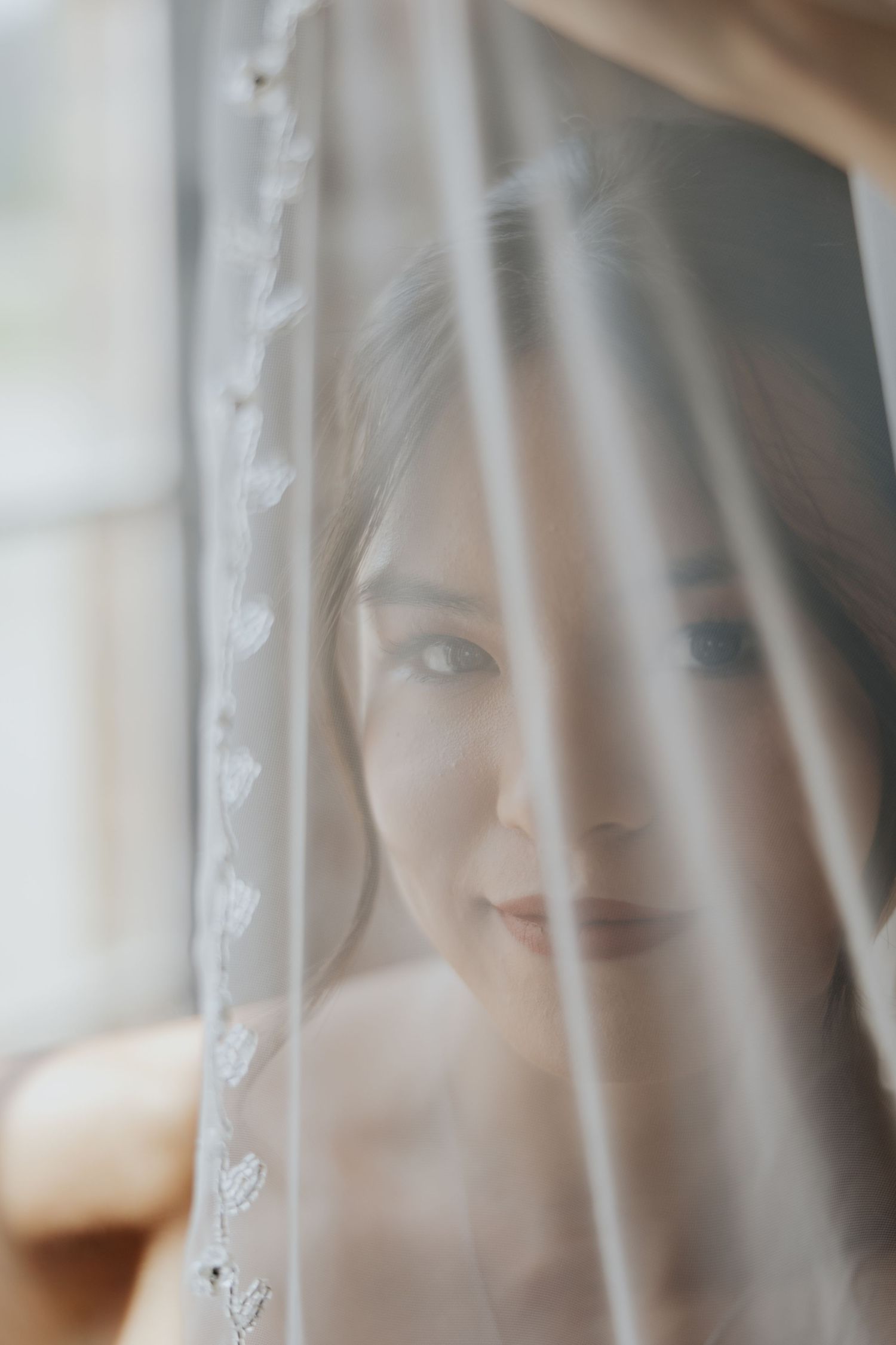 Ethereal bridal portrait of bride peeking through delicate floral embroidered wedding veil.