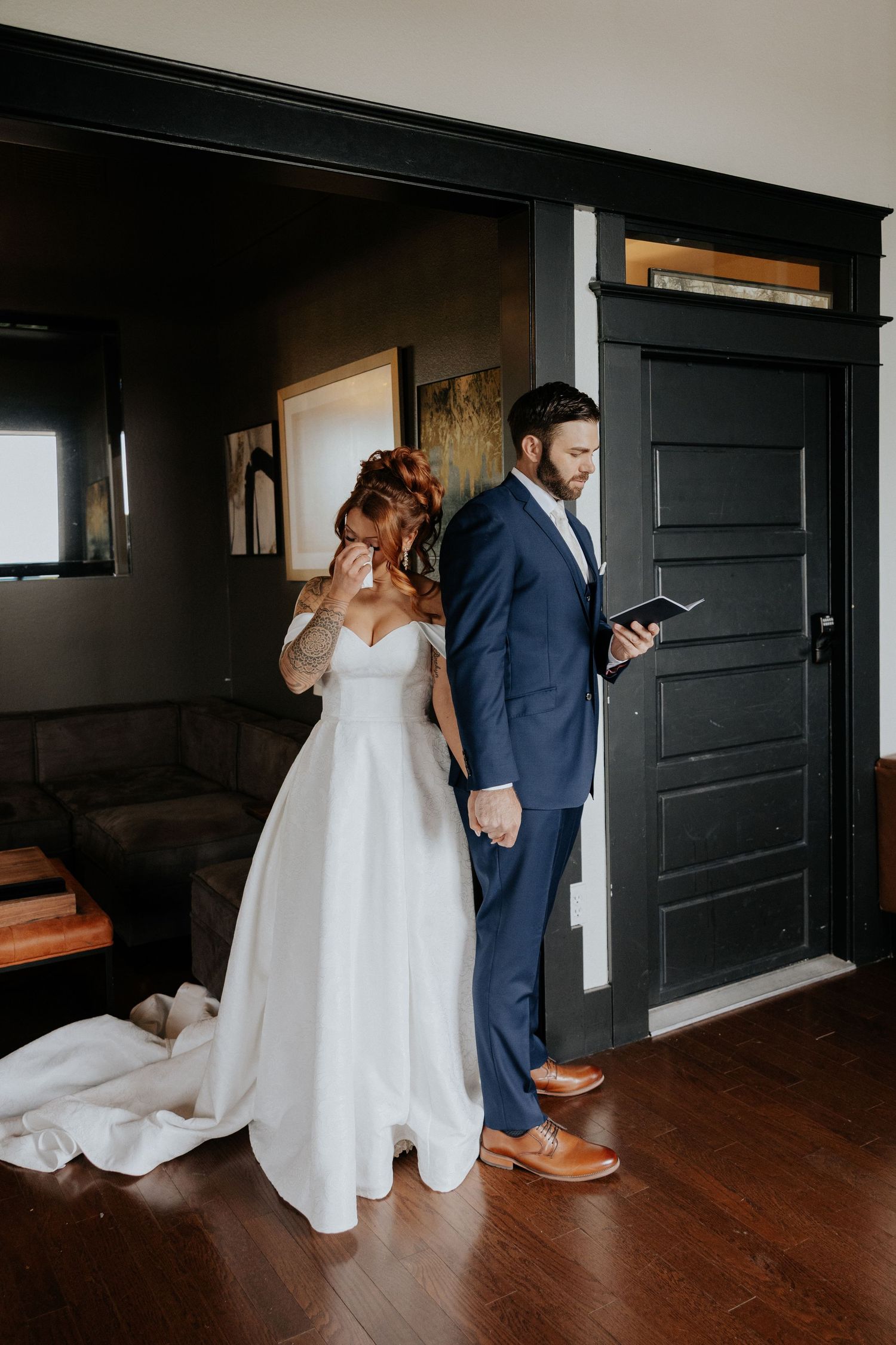 Emotional bride wiping tears while groom reads vows back-to-back in dark interior wedding venue.